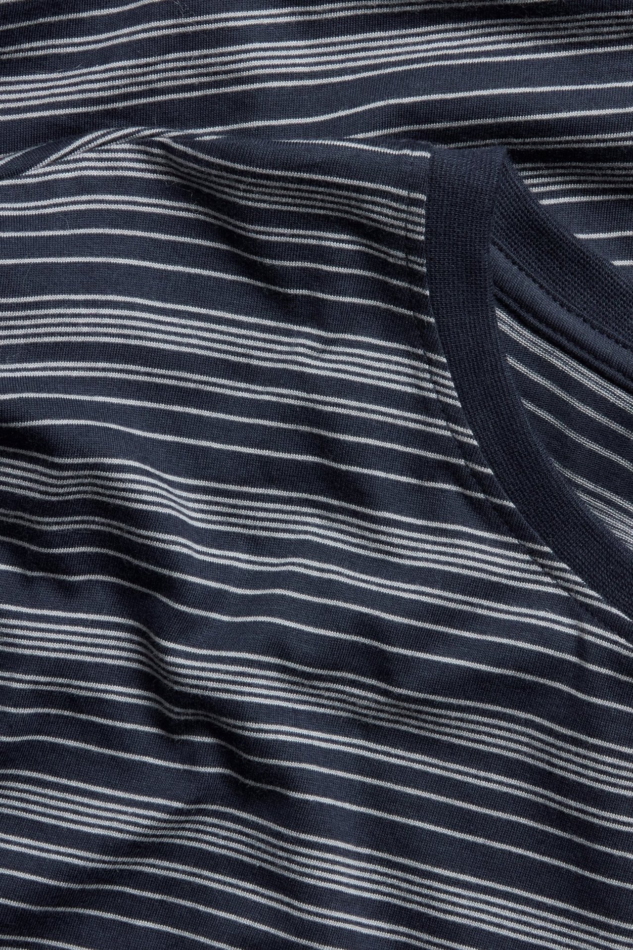 Zbliżenie na granatową piżamową koszulkę z bawełnianej dzianiny w białe paski z prążkowanym dekoltem.