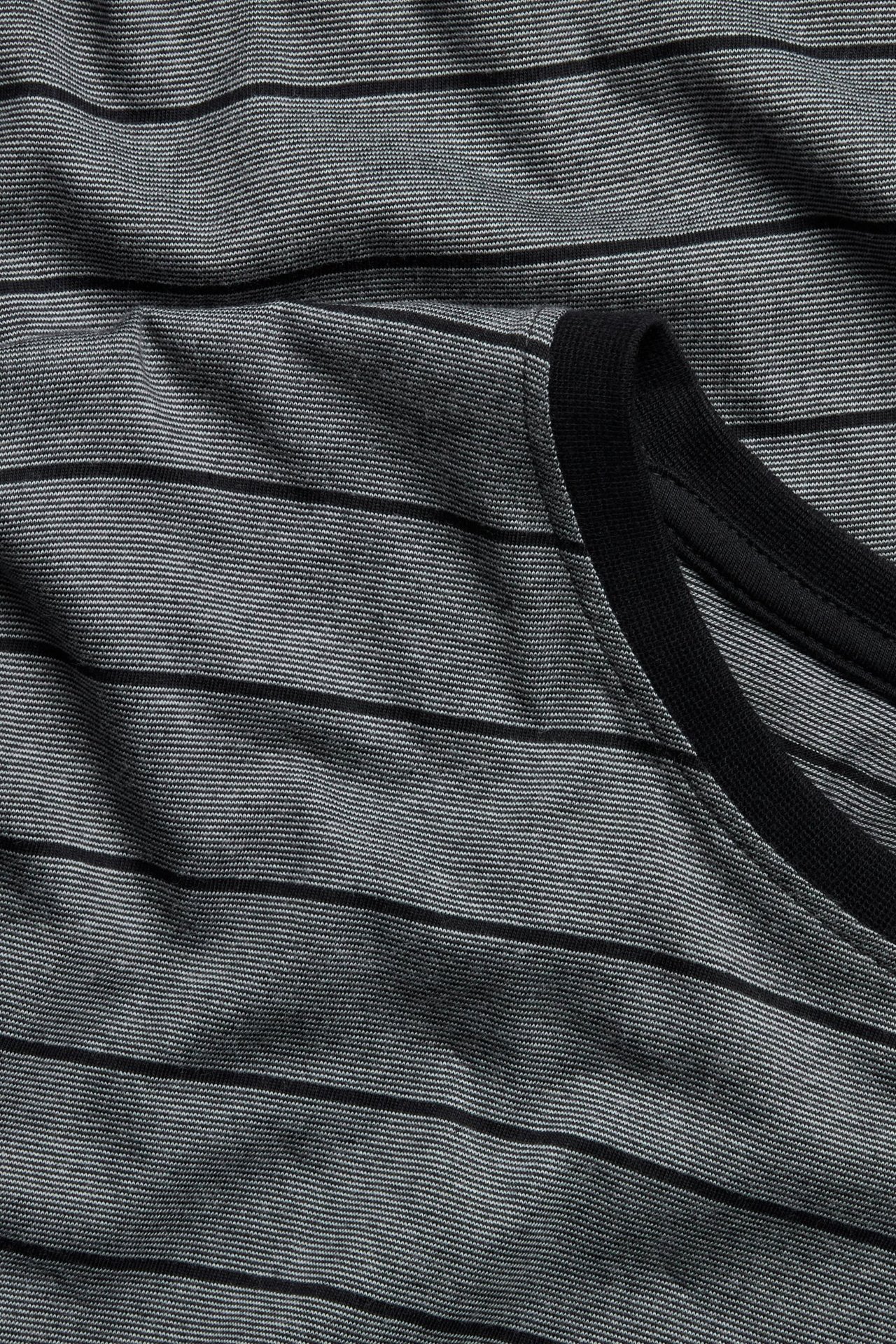 Zbliżenie na pasiastą piżamową bluzkę: czarno-jasnoszary dżersej z czarnym ściągaczem.