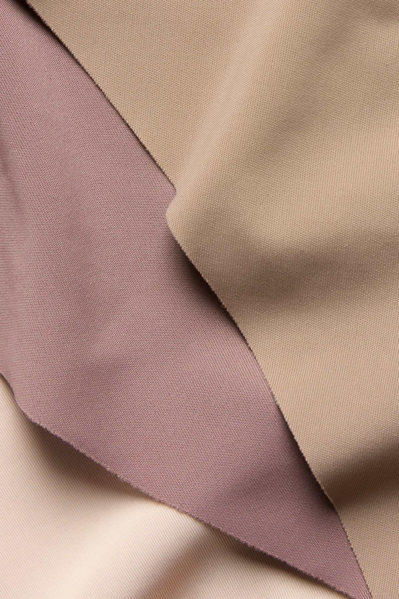 Nærbilde av tre glatte, ensfargede stoffprøver: mørkrosa, beige og lys beige.
