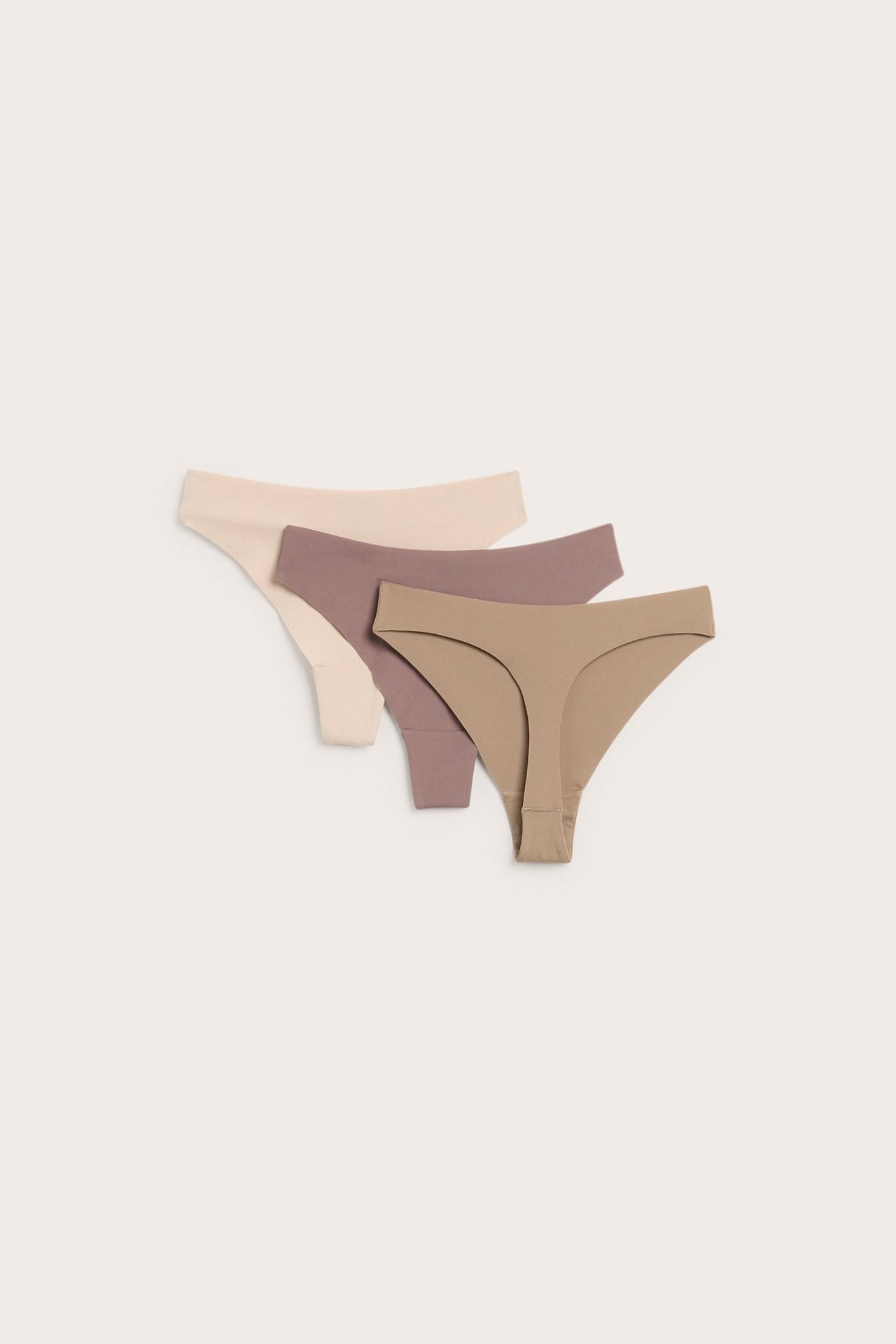 Flat lay-visning av tre sømløse damestringtruser i lys beige, mauve og lysbrun.