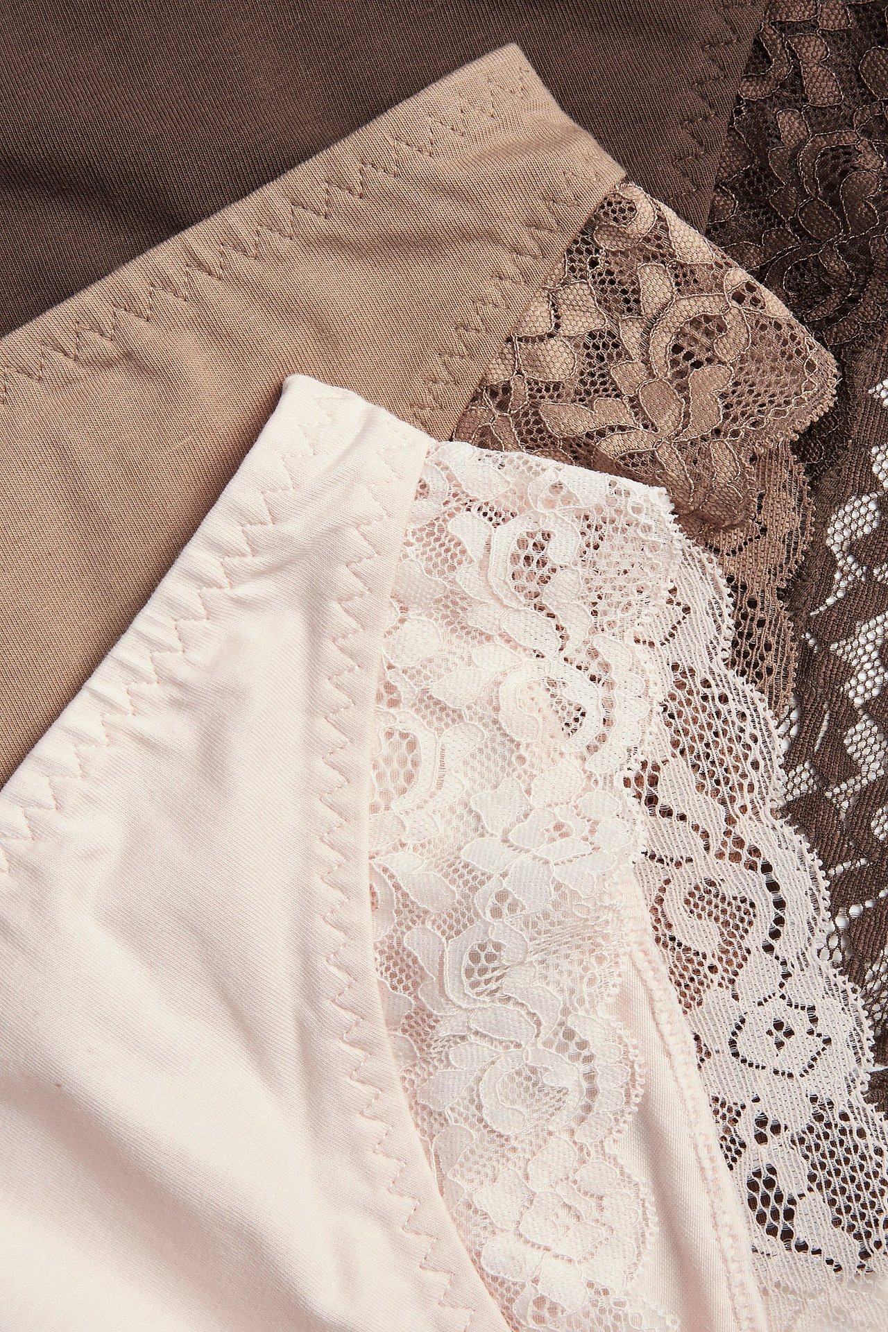 Nærbilde av tre brazilian truser for dame: lys rosa med blonder, beige og mørk brun med blonder.