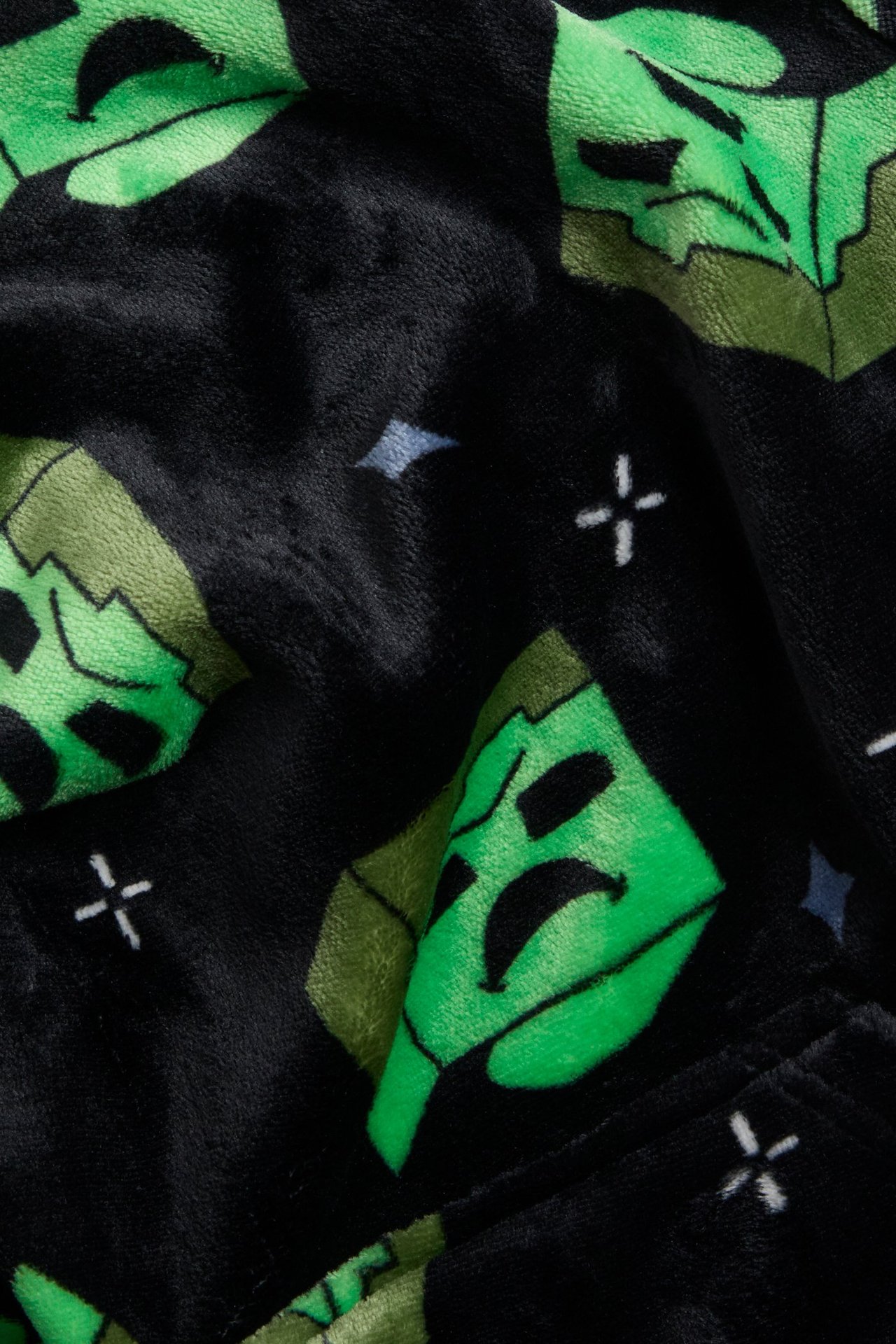 Närbild av svart fleecehoodie-tyg med grönt Minecraft Creeper-mönster.