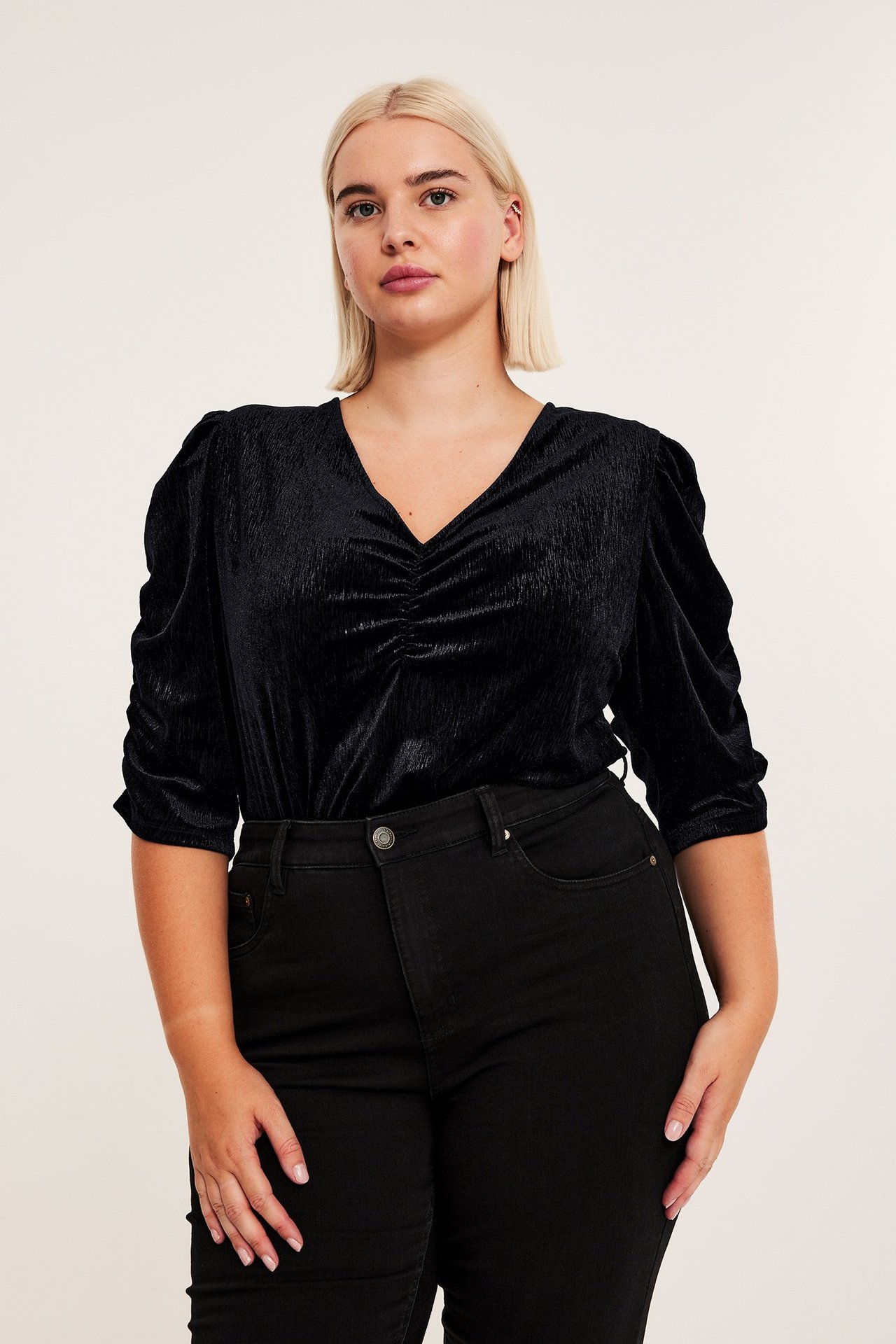 Przód: kobieta w czarnej welurowej bluzce z dekoltem V, marszczonymi rękawami 3/4 i czarnych jeansach.