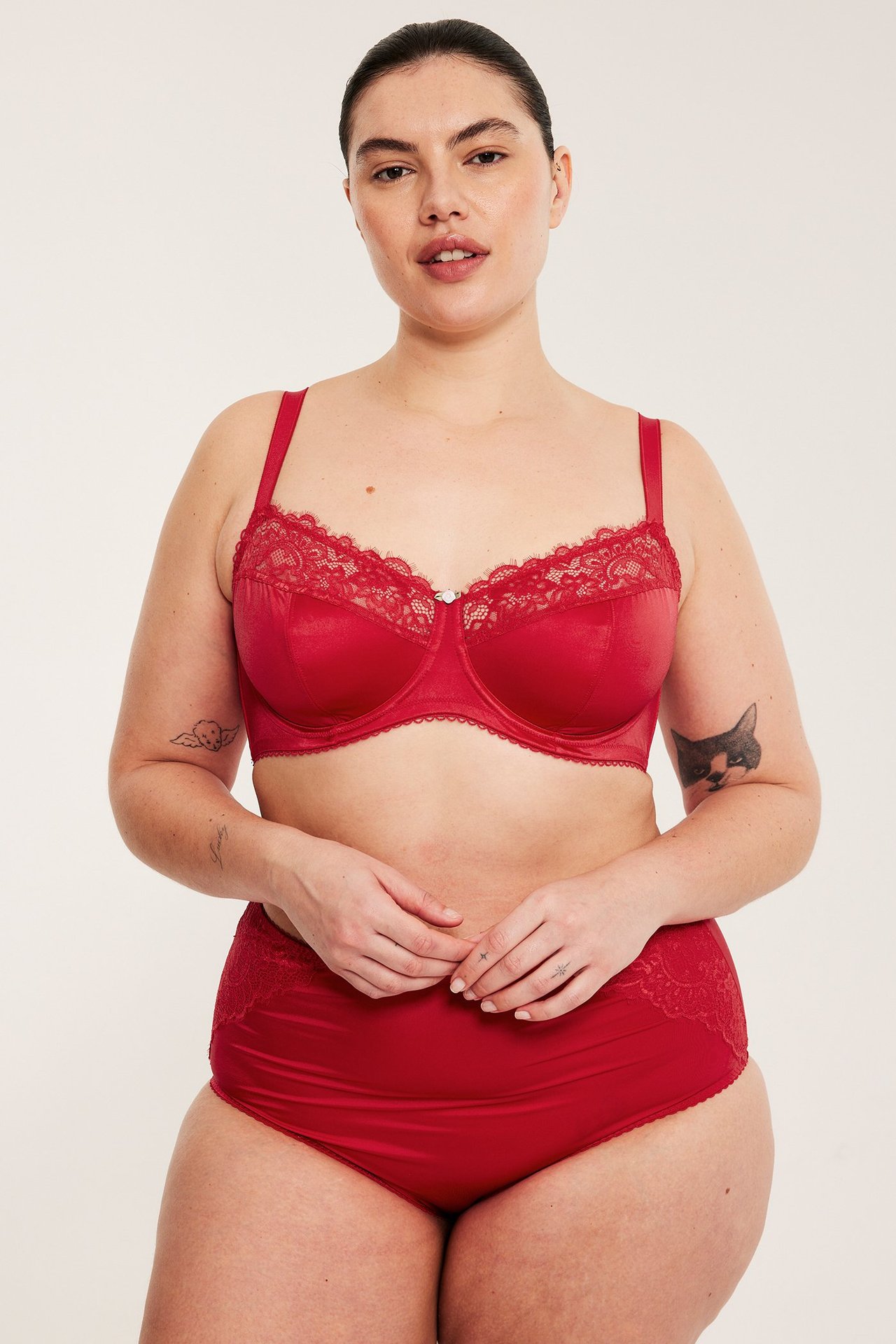 Frontvy av kvinna i röd bygel-bh i satin med spetskant och matchande röda trosor med spets.