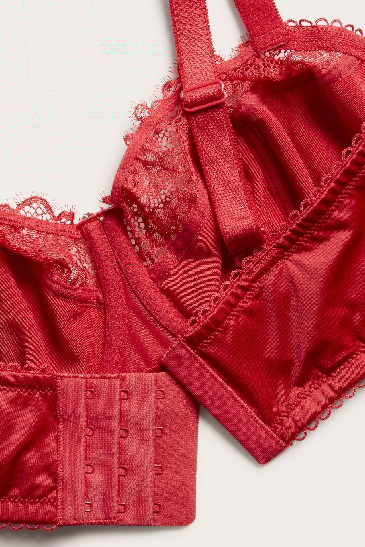 Nærbilde av en rød bøyle-BH i sateng med blondekant, justerbare stropper og hektelukking.