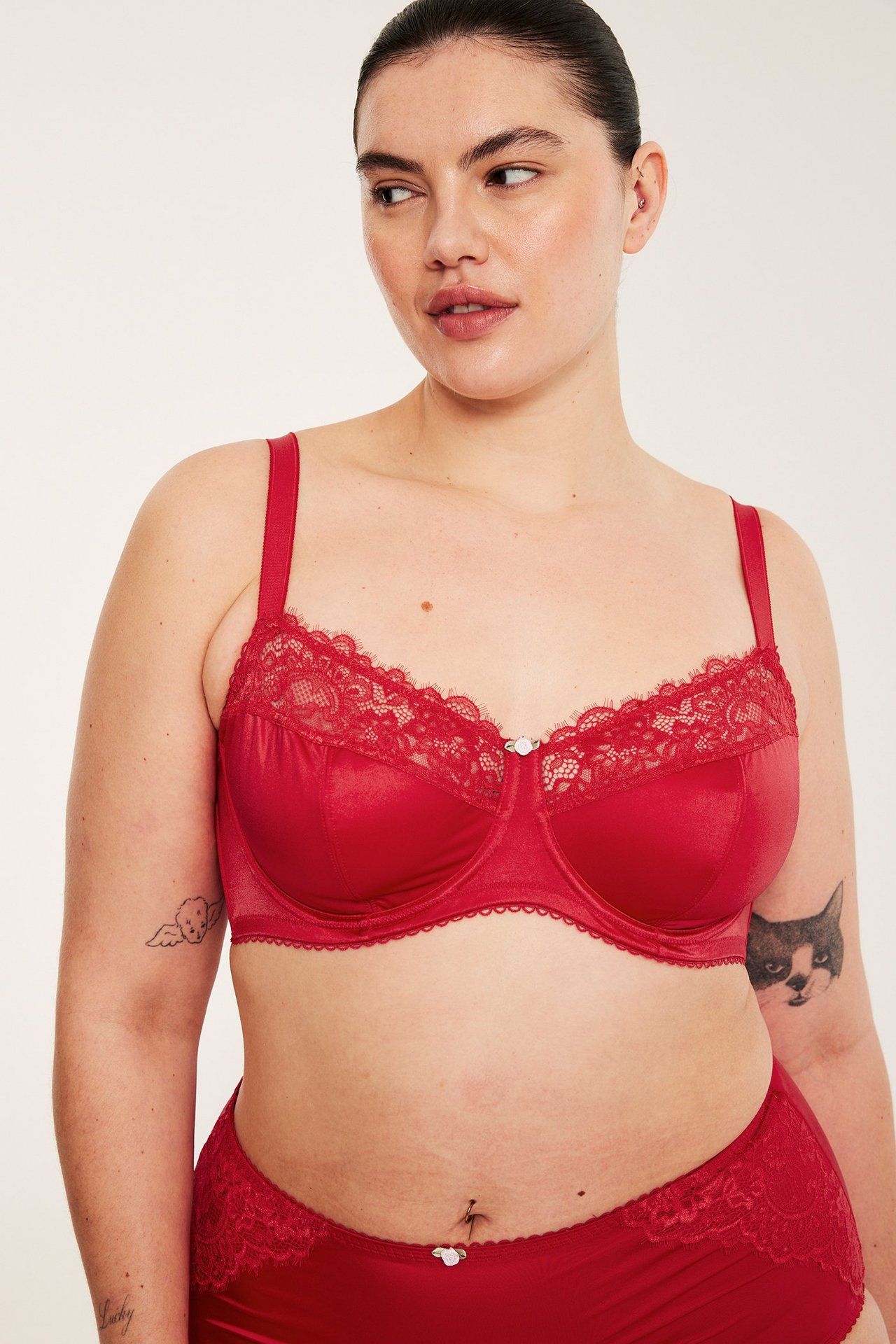 Framifrån, kvinna i röd satinbygel-bh med spetskant och matchande röda satintrosor.