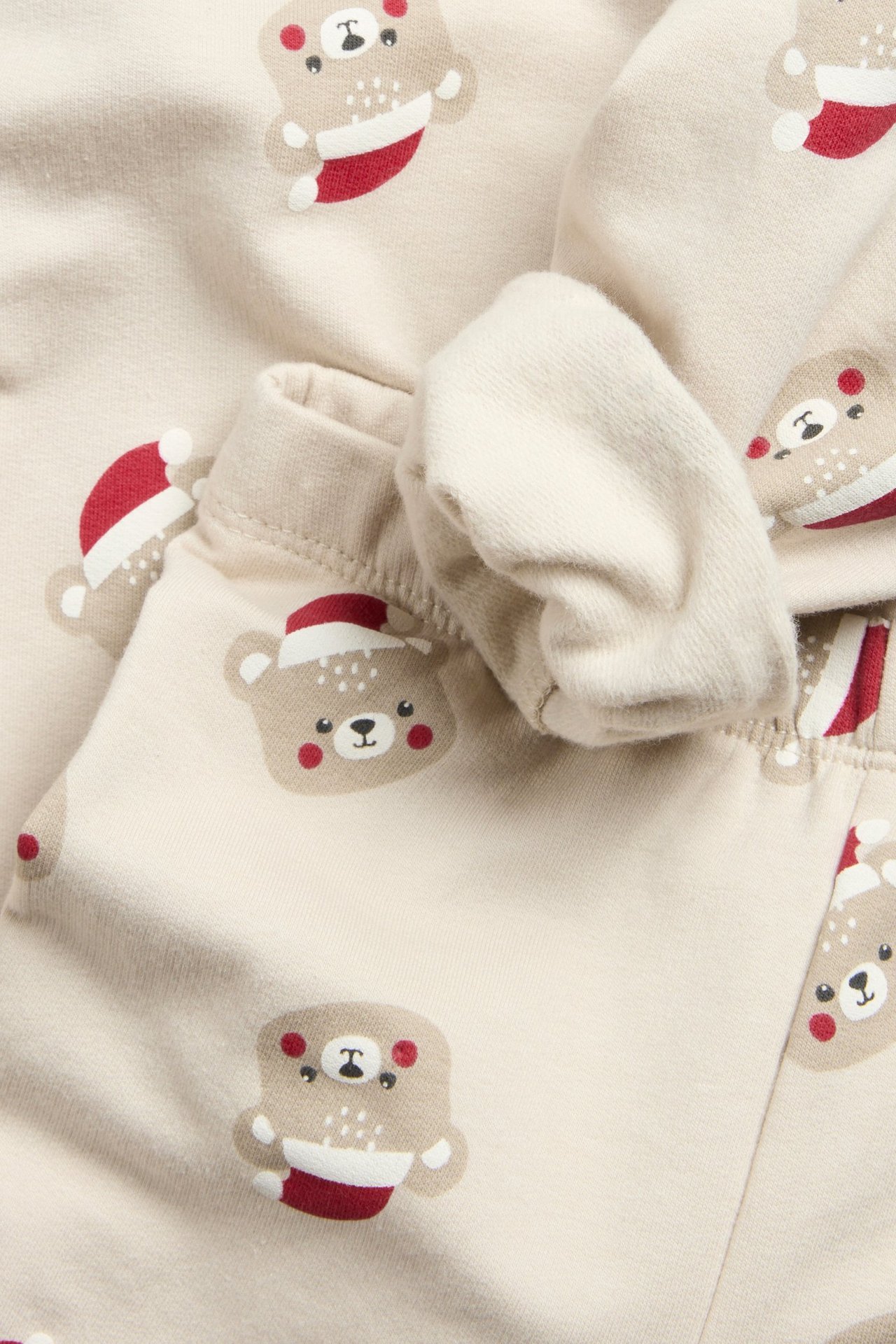 Zbliżenie beżowego dziecięcego kompletu dresowego z bluzą i legginsami w świąteczny wzór misia.
