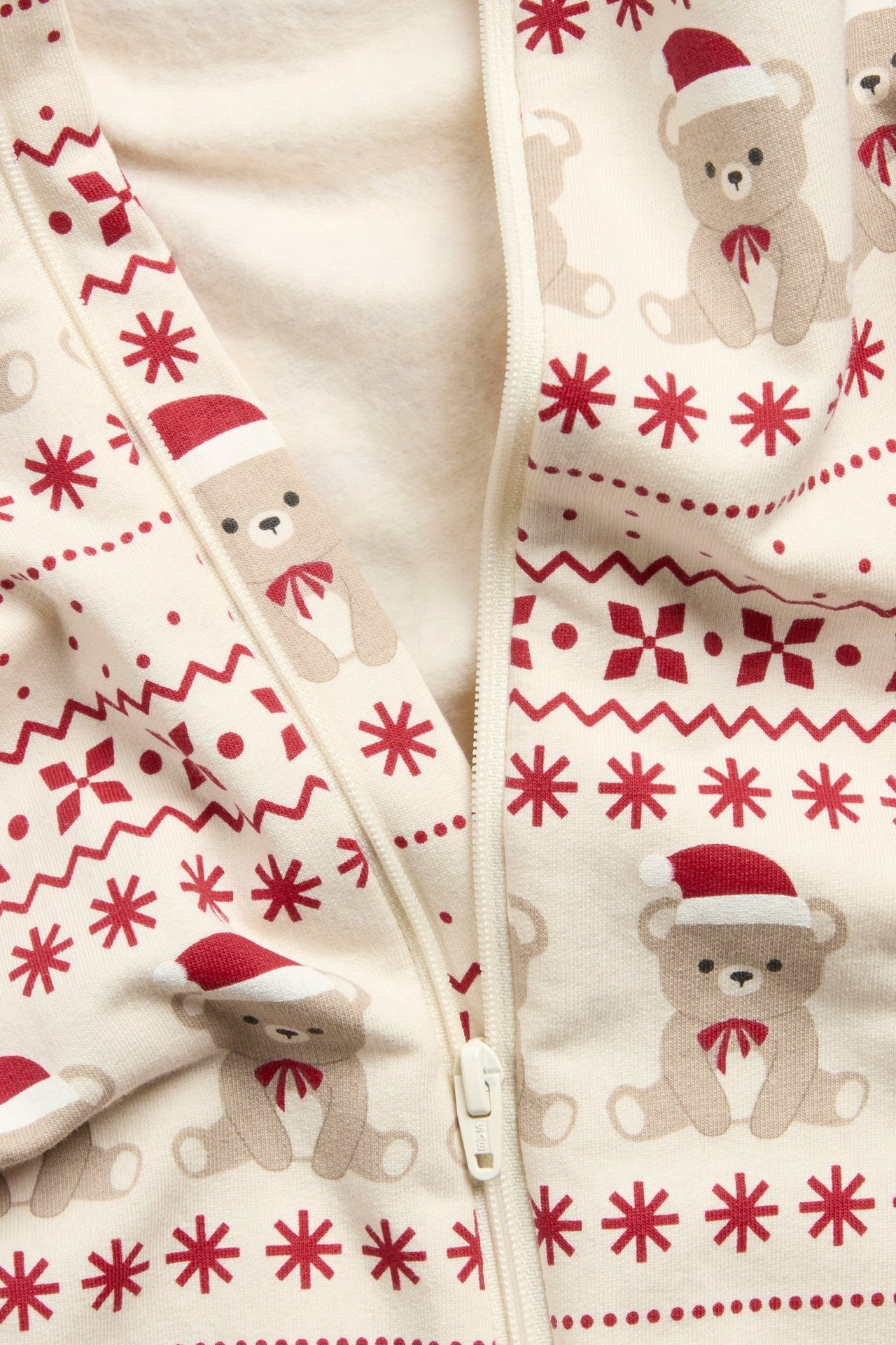 Zbliżenie na beżowy pajacyk niemowlęcy z nadrukiem czerwonych świątecznych misiów i zamkiem z przodu.