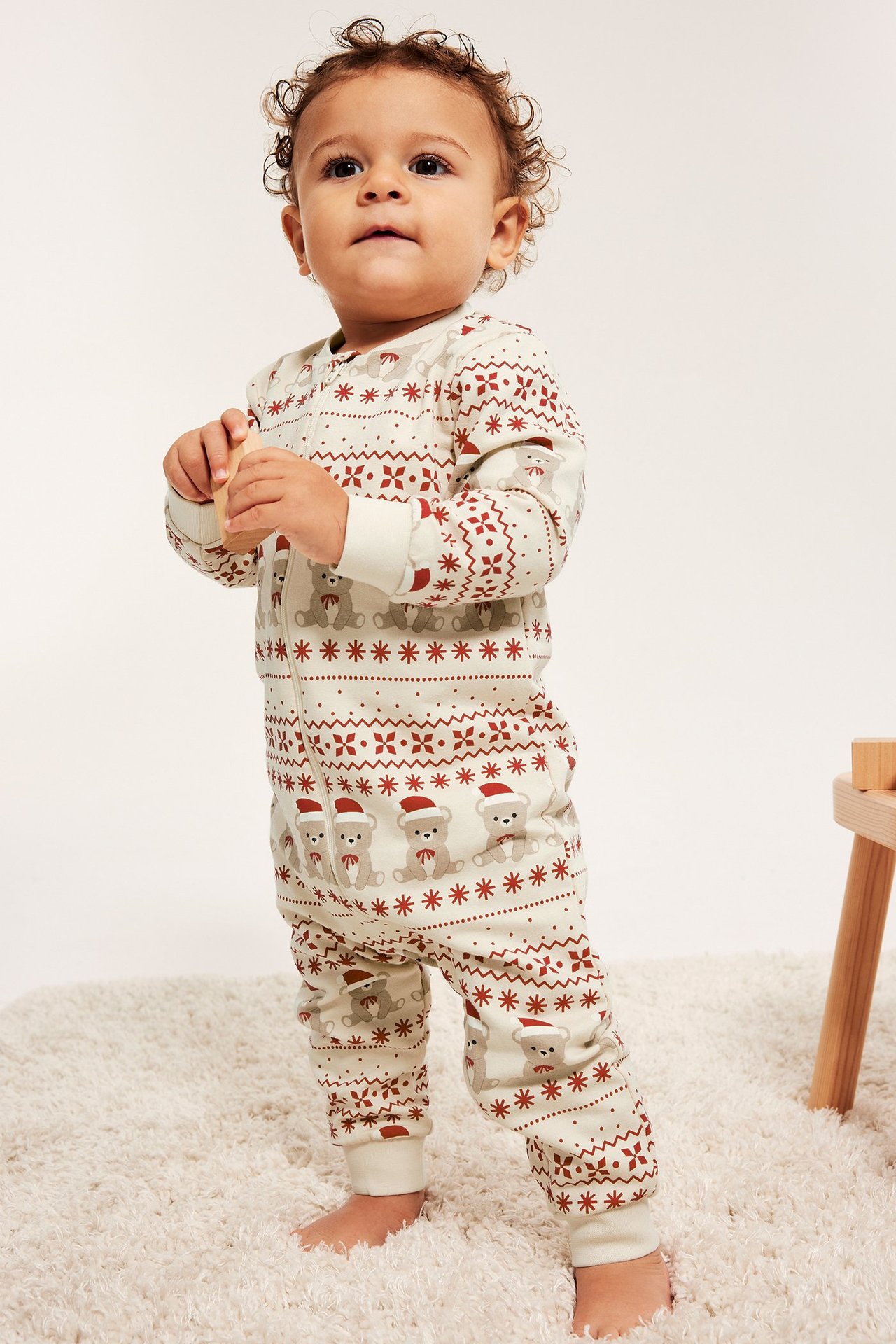 Baby i lys beige juleonesie i sweatshirt-kvalitet med rødt mønster, frontvisning.