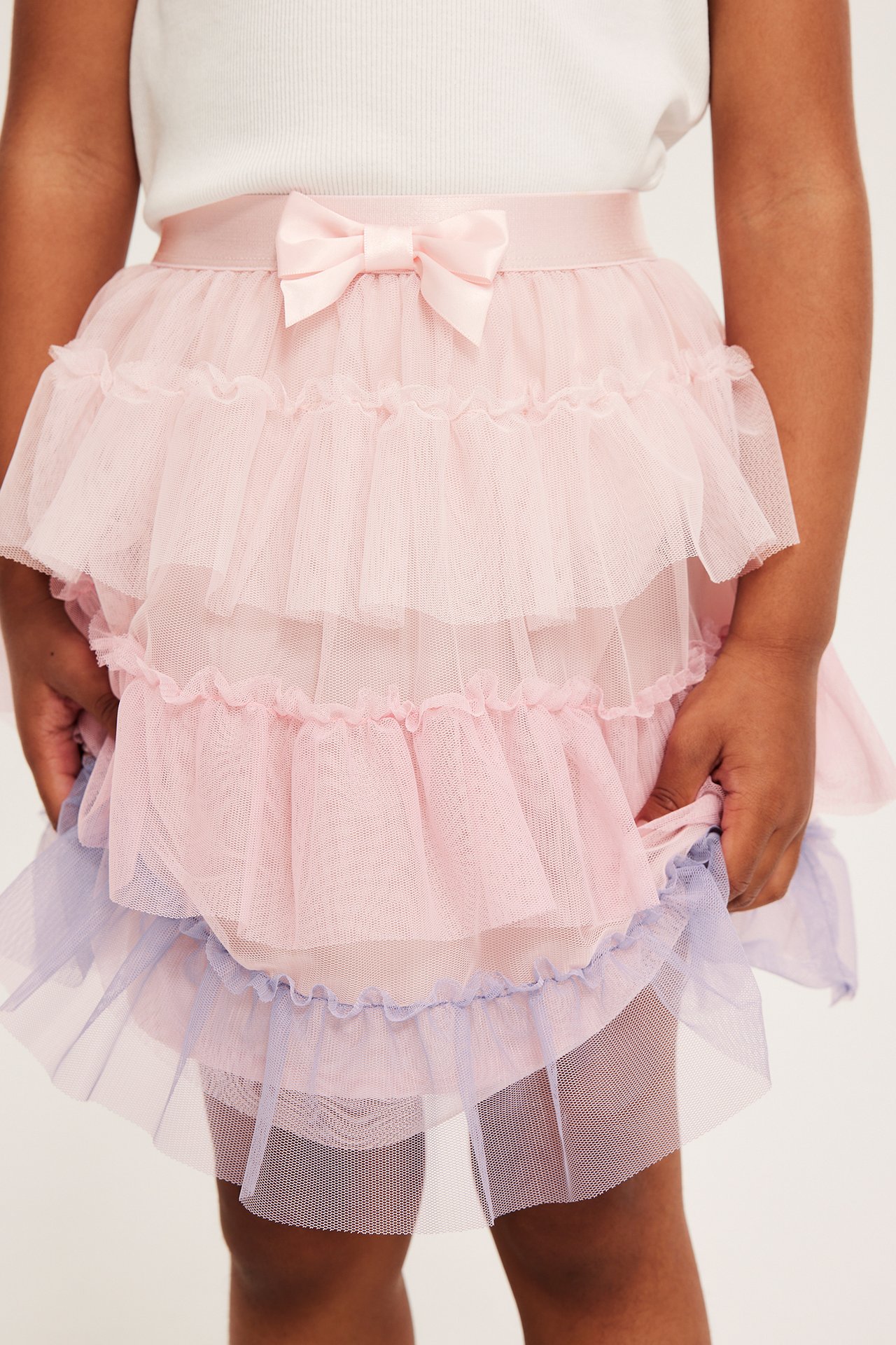 Framifrån: Barn i rosa volangkjol av tyll med satinrosett, lila nederkant och vit topp.