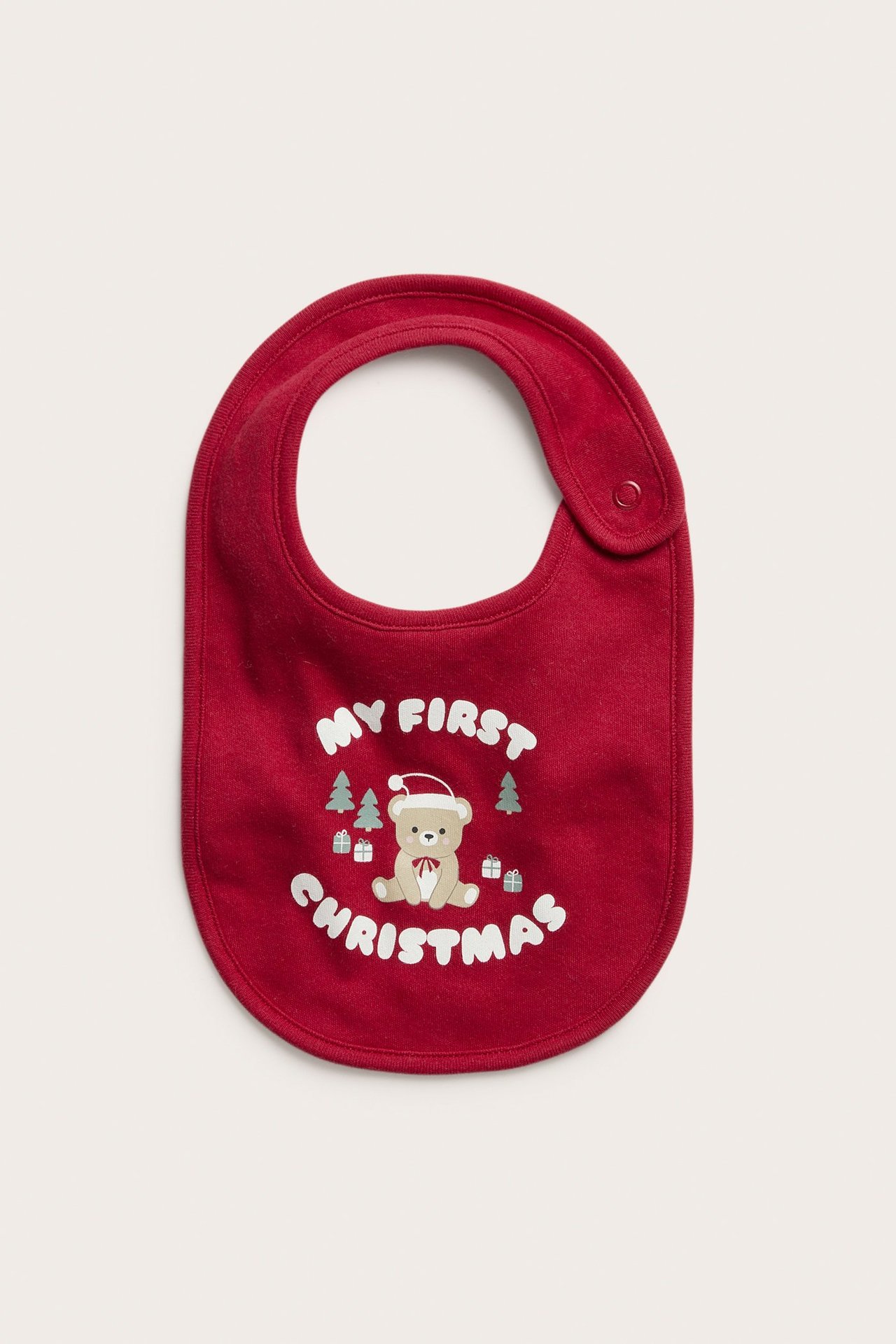 Edestä: punainen puuvillainen vauvan ruokalappu 'My First Christmas' -painatuksella ja nepparikiinnityksellä.