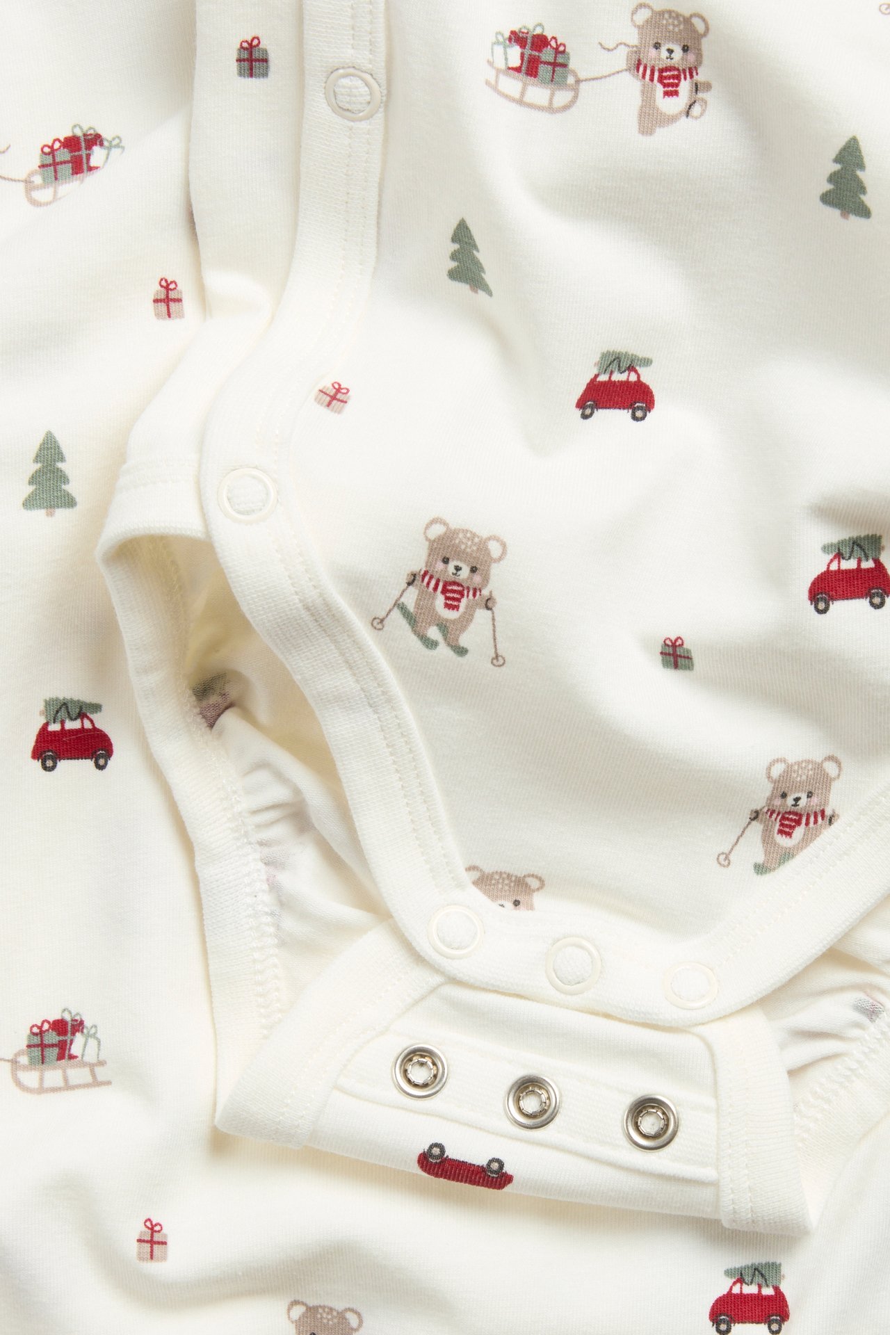 Nærbilde av en offwhite langermet babybody med julemønster og trykknapper.