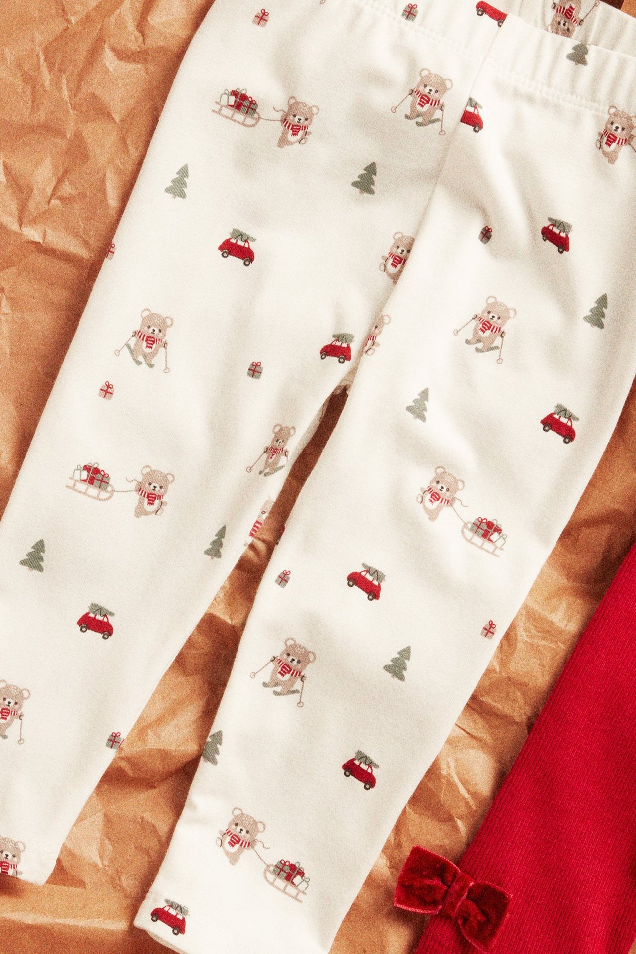 Lähikuva lasten luonnonvalkoisista leggings-housuista, joissa jouluisia karhuja, autoja ja lahjoja.