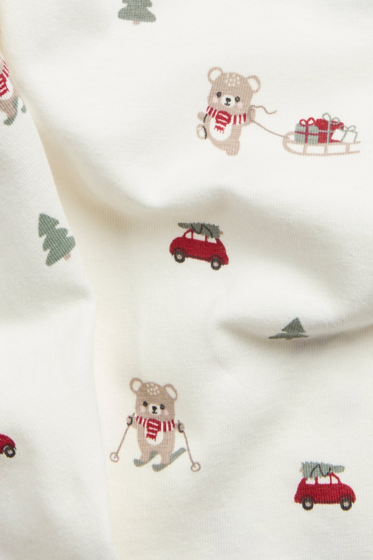 Zbliżenie na kremowe legginsy z mieszanki bawełny z świątecznym nadrukiem misiów i samochodów.