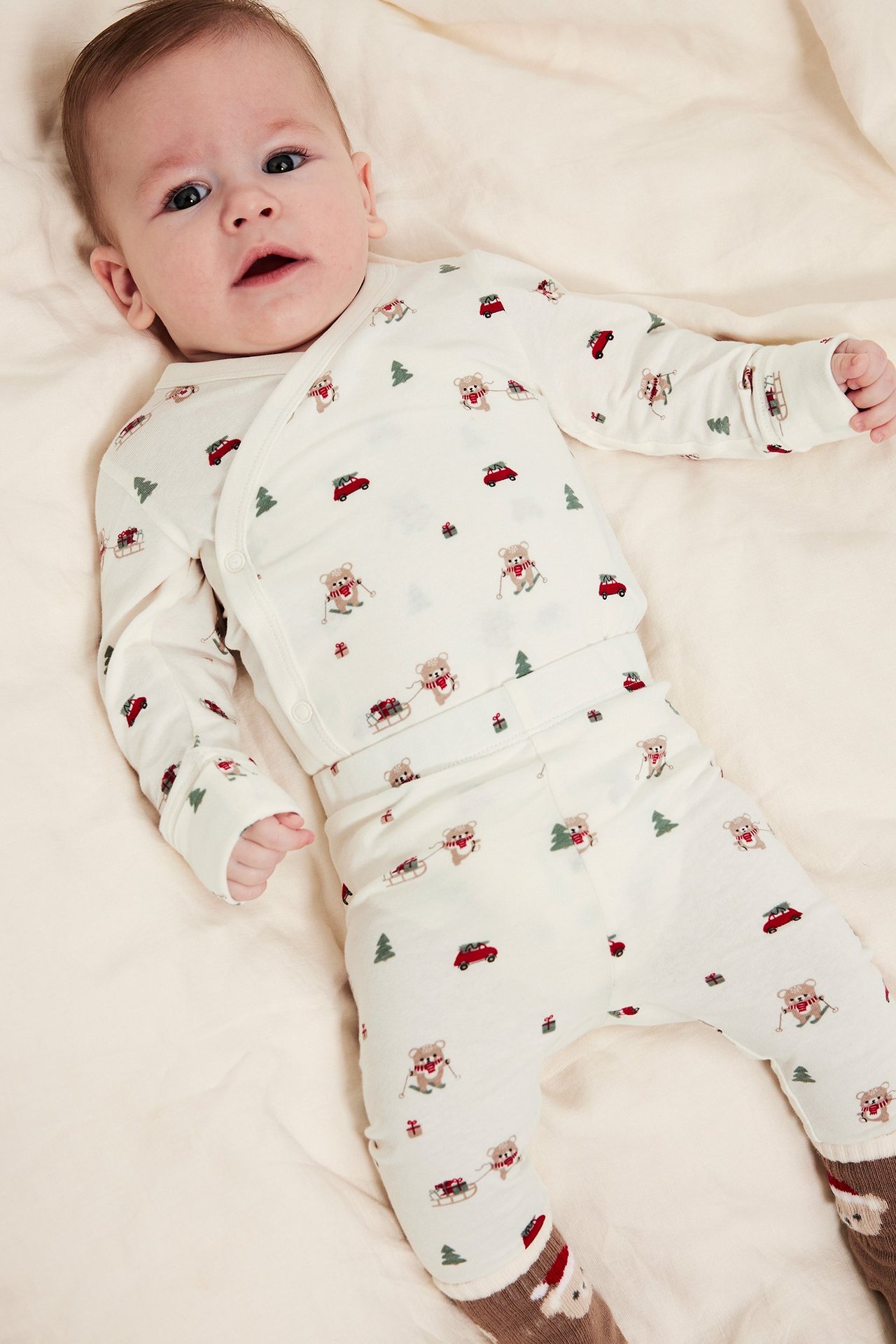 Baby i julemotivsleggings i offwhite, ligger på seng, elastisk midje.