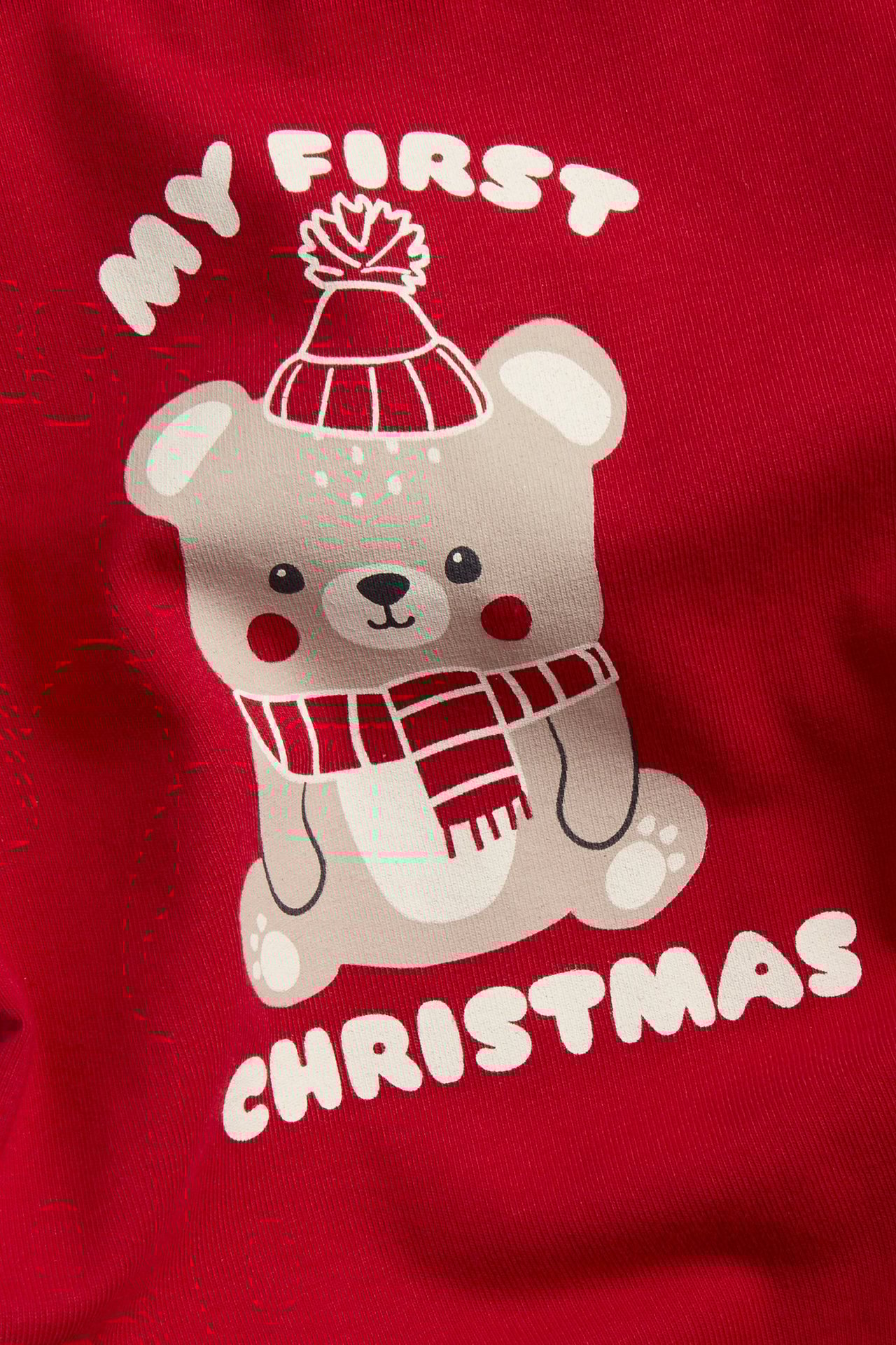 Nærbilde av en rød langermet babybody med julebamsetrykk og teksten 'MY FIRST CHRISTMAS'.