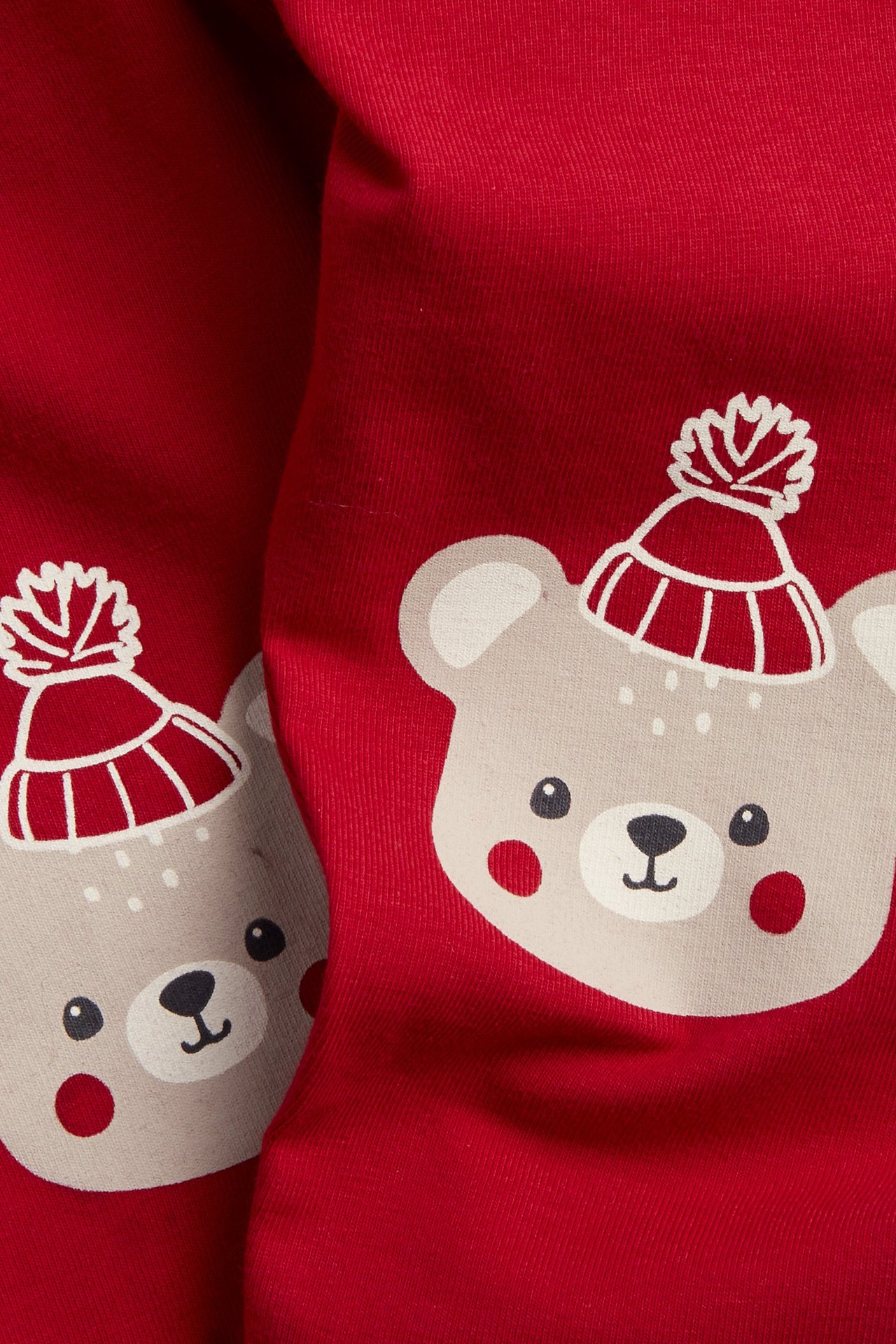 Närbild av röda babyjersey-leggings med ljusbeige björnprint i röd och vit stickad mössa.