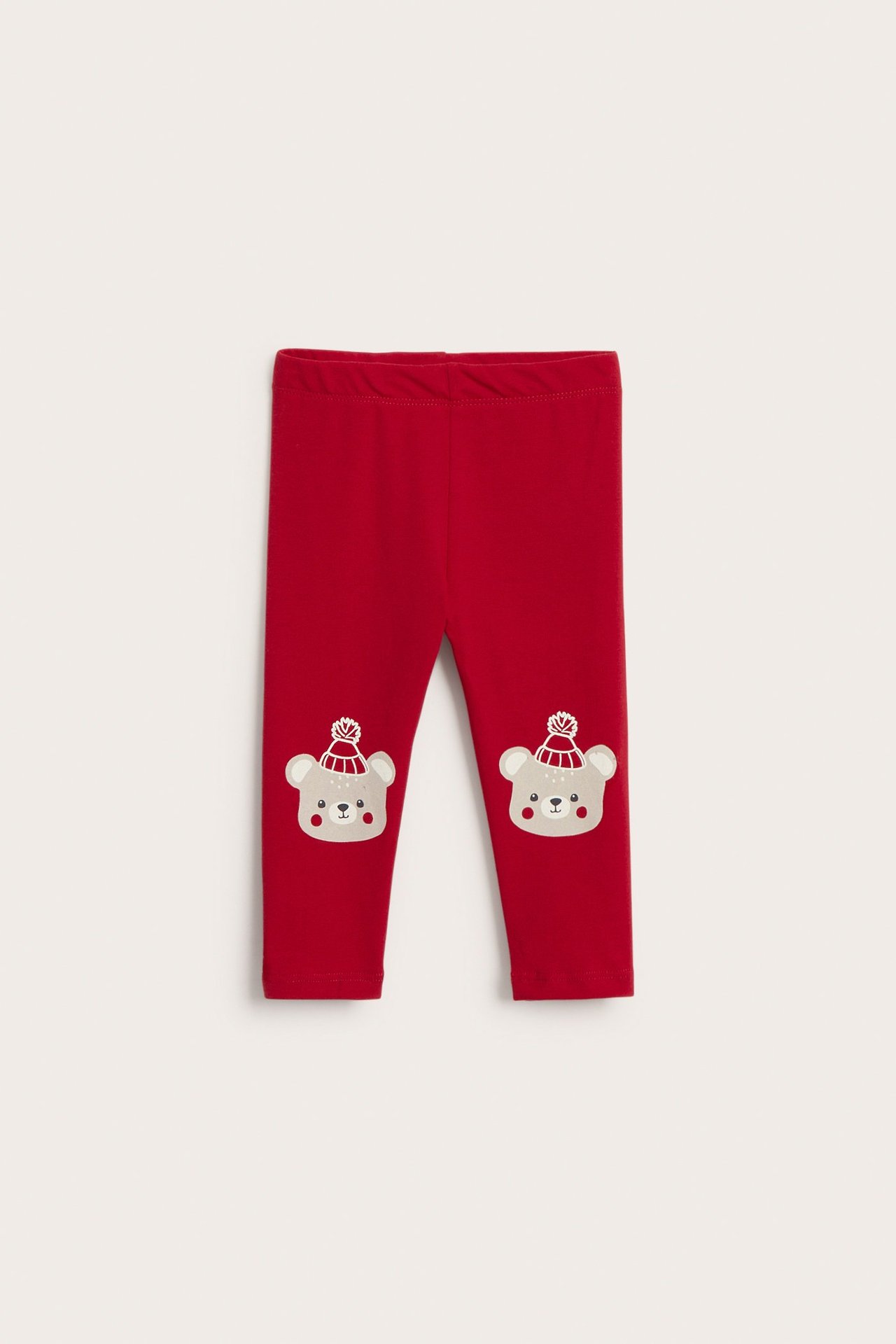 Frontvy av babyröda leggings i bomullsblandning med björnprint med vintermössor på knäna.