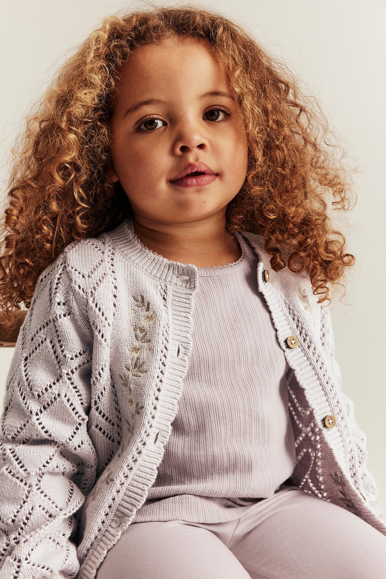 Forfra: Barn i lys lilla mønsterstrikket bomullskofta med broderte blomster, over matchende ribbet topp og leggings.