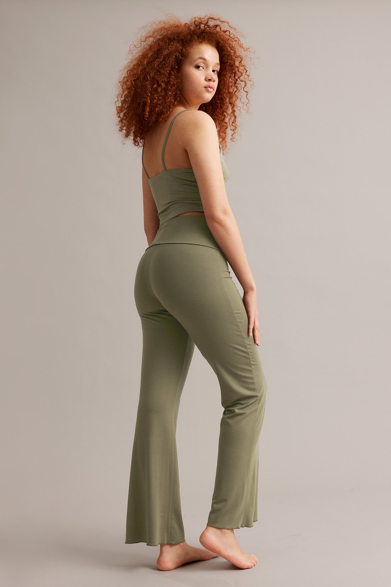 Side-bakfra visning av kvinne i khakigrønn viskose bootcut loungebukse med matchende camisole-topp.
