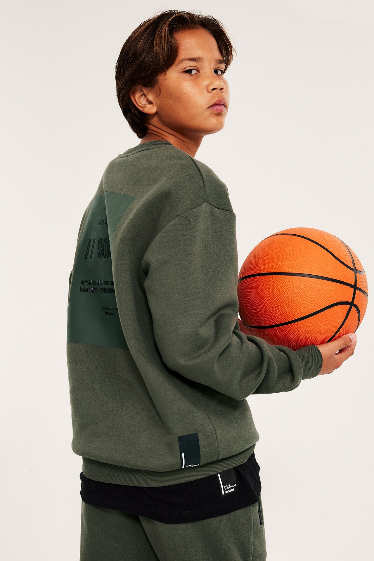 Chłopiec w zielonej bluzie z nadrukiem z przodu, trzyma piłkę, widok z przodu.