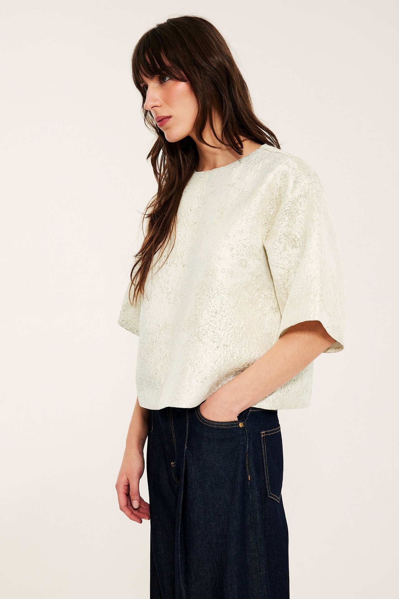 Sidebilde av en kvinne i offwhite jacquardmønstret bluse og mørkeblå vide jeans.