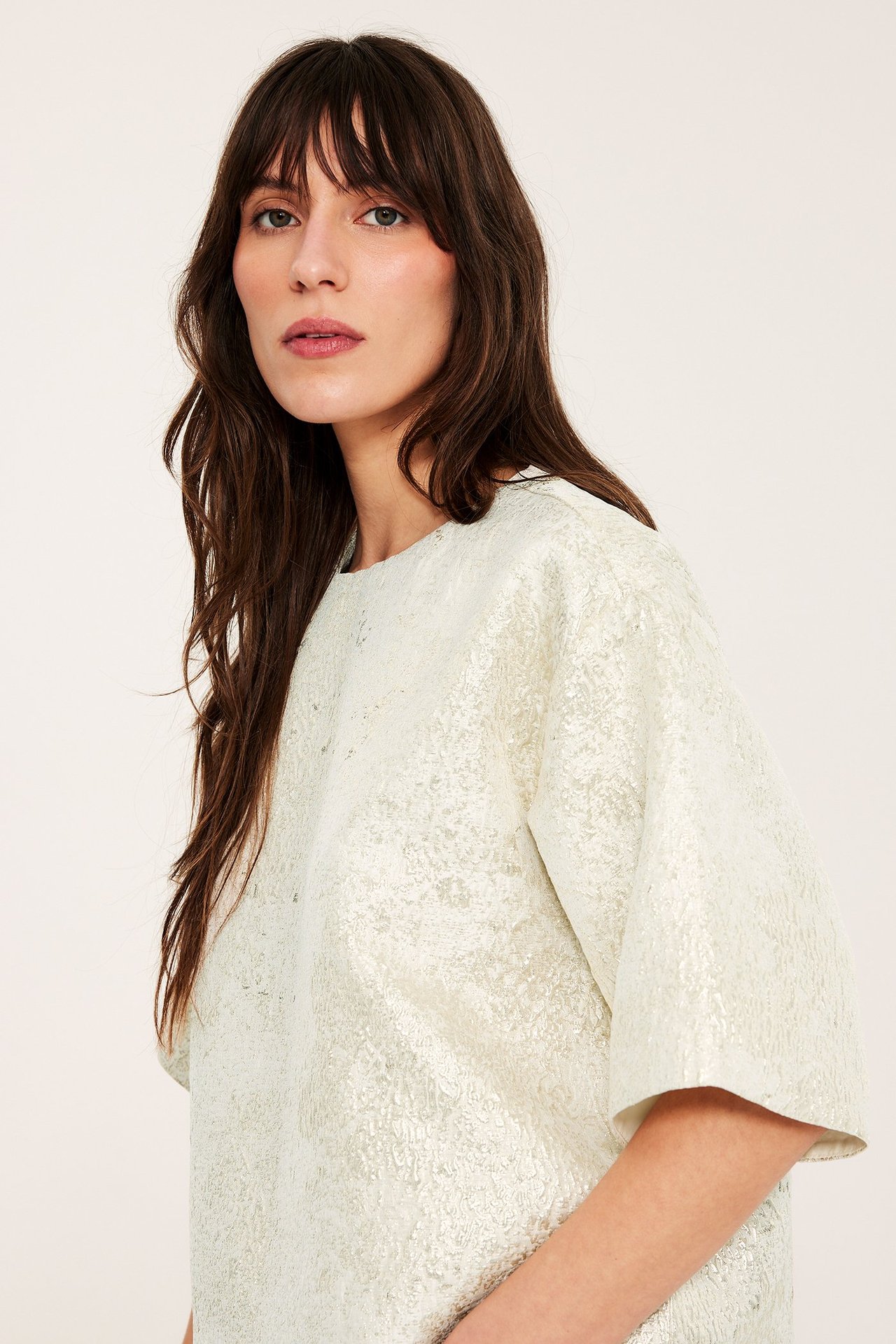 Nærbilde forfra: kvinne i offwhite jacquardmønstret bluse med rund hals og korte, vide ermer.