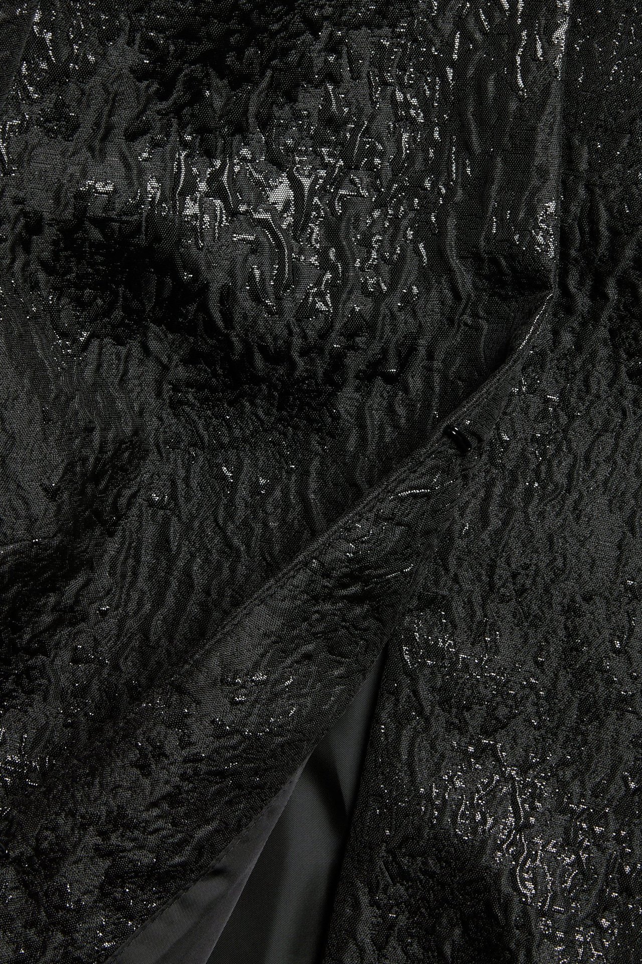 Zbliżenie czarnej bluzki żakardowej z teksturowanym wzorem i ukrytym zapięciem z przodu.