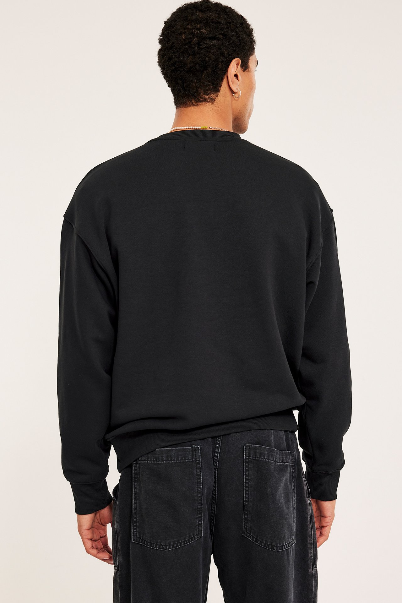 Mann i svart oversized-genser med droppet skulder og svarte jeans, front