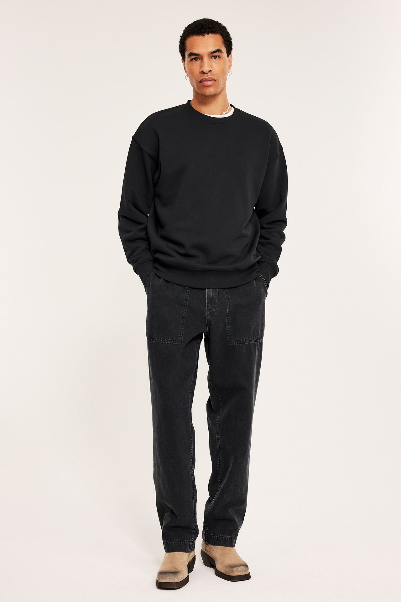 Forfra: mann i svart oversized sweatshirt, mørkegrå avslappede bukser og beige sko.