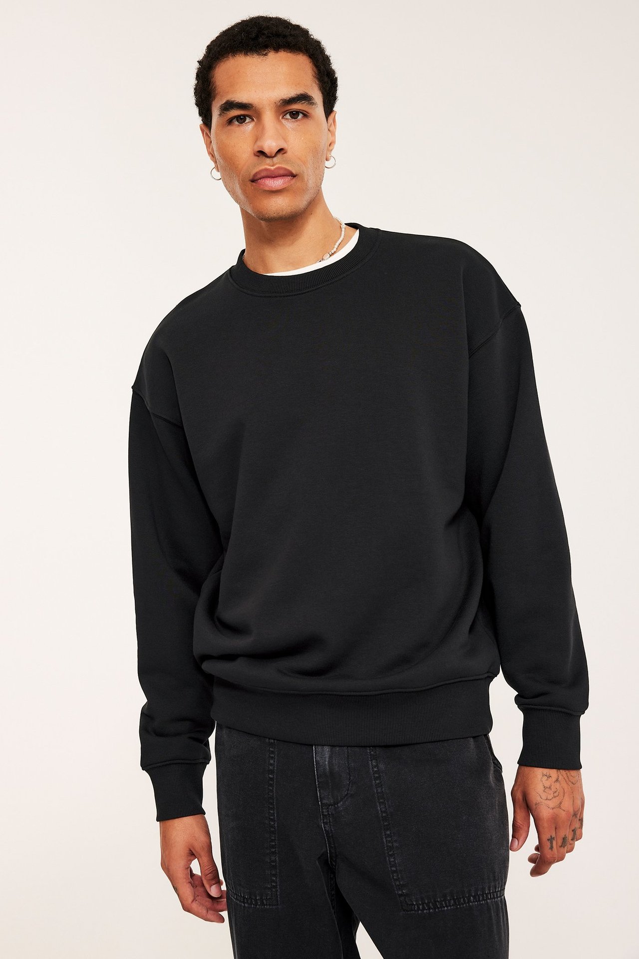 Frontvy av en mann i en svart oversized sweatshirt over en hvit t-skjorte, med mørkegrå bukser.
