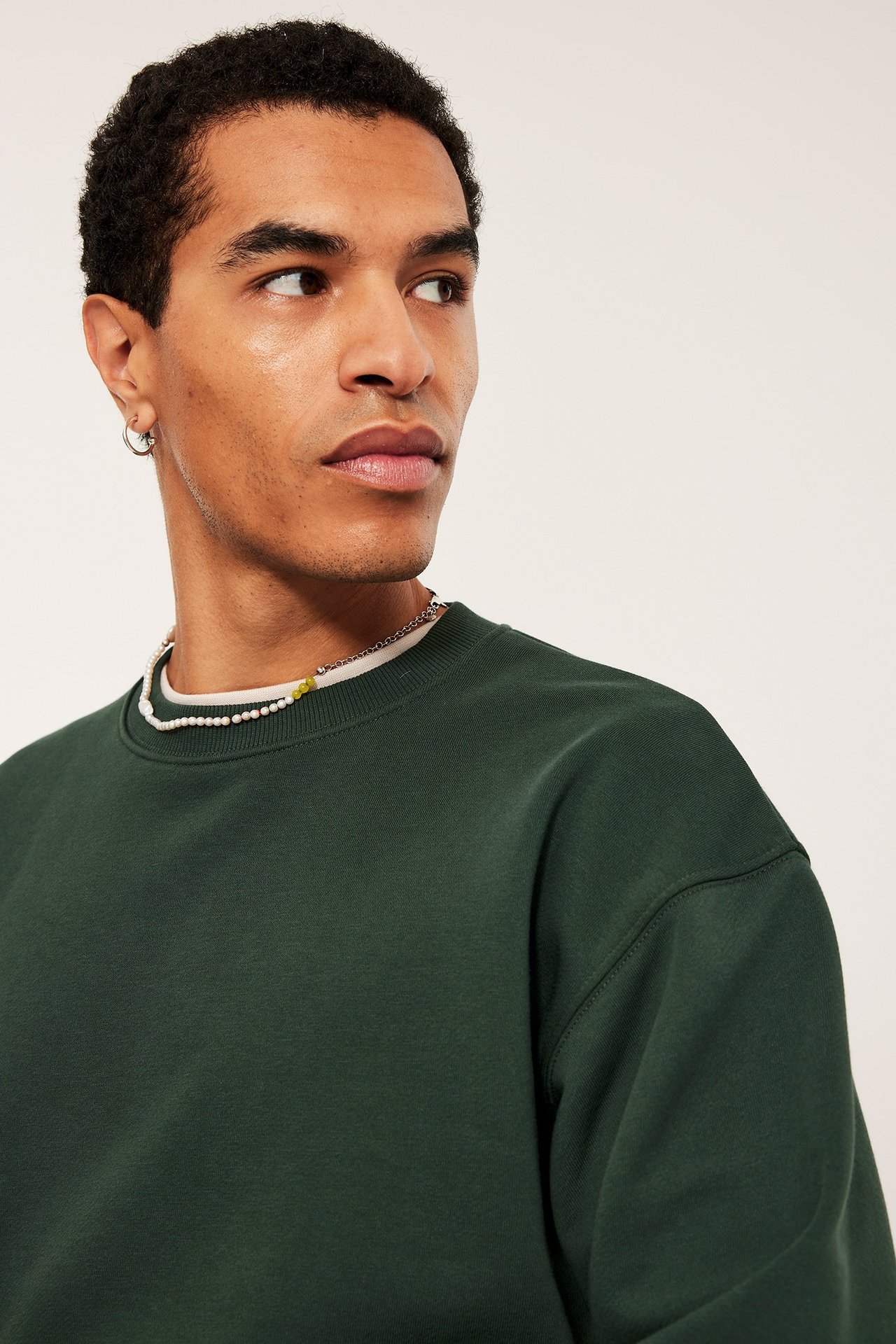 Mann i grønn oversized-genser med droppet skulder, enkel og ensfarget.
