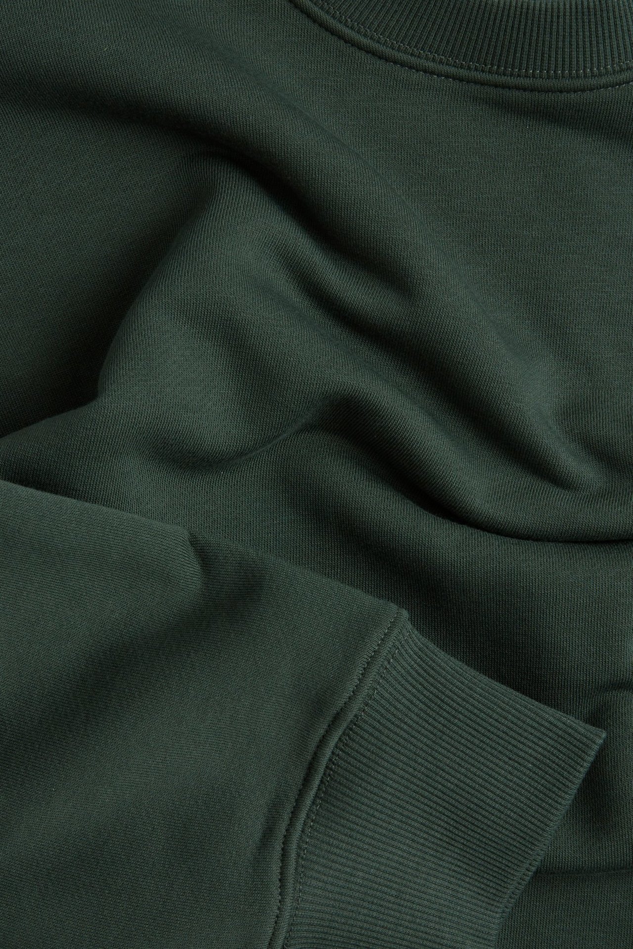 Zbliżenie na ciemnozieloną, oversize'ową bluzę z mieszanki bawełny z prążkowanym dekoltem i mankietem.