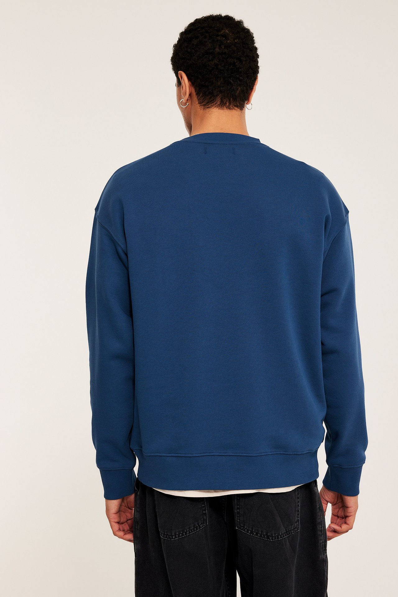 Bakifrån, en man i blå oversized sweatshirt över vit t-shirt och mörka jeans.