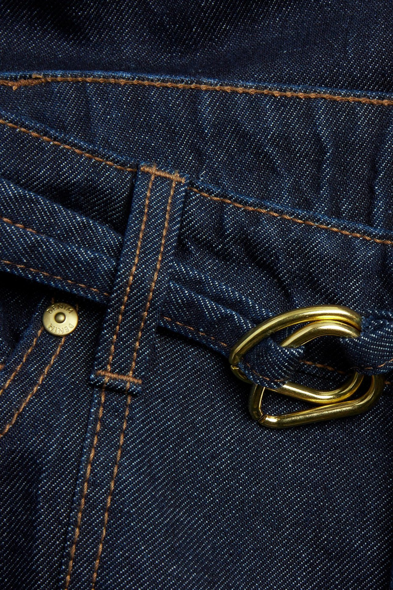 Närbild av mörkblå denimjeans med hög midja, matchande bälte och guldtonat dubbelringat spänne.