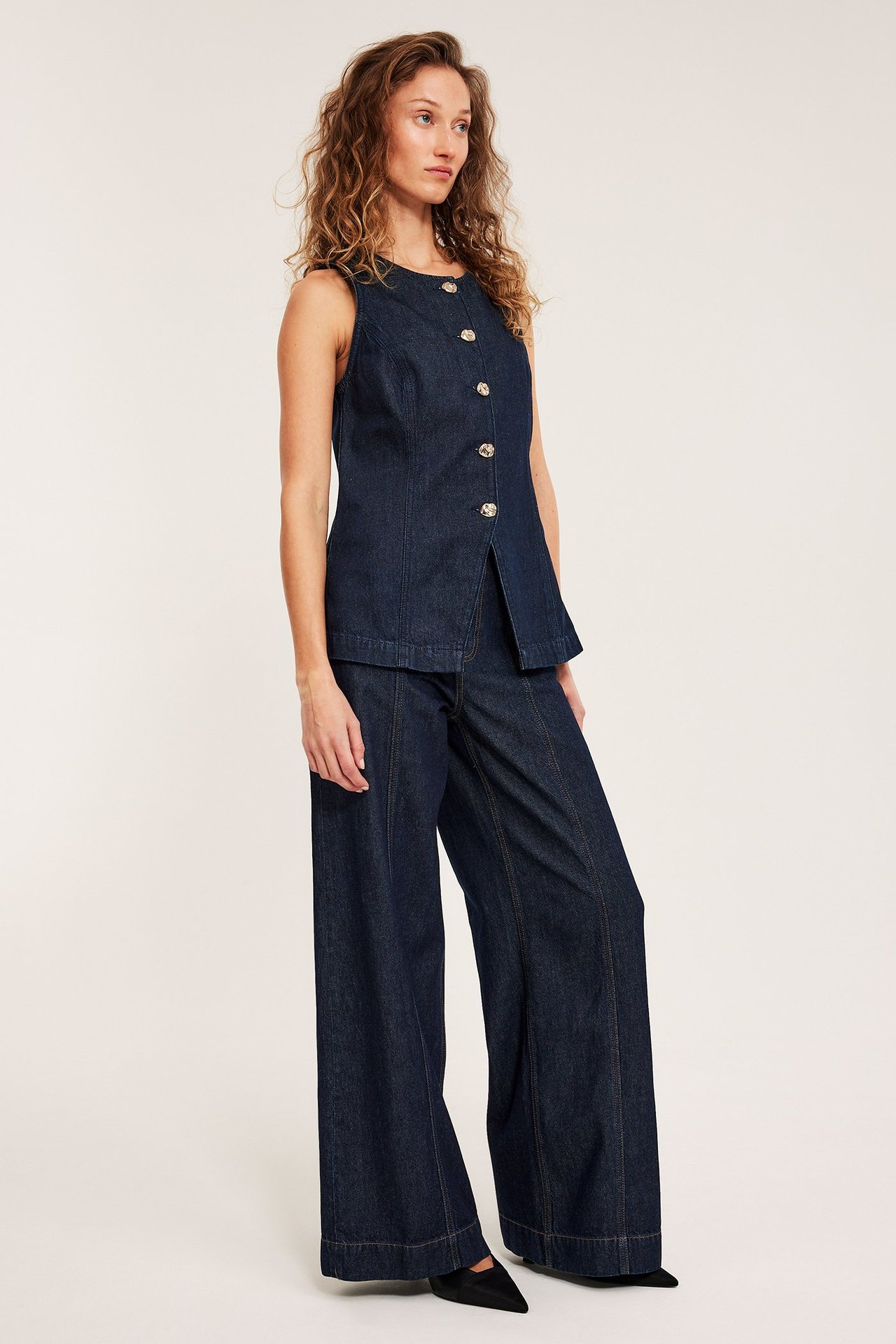 Nainen tummissa leveissä korkeavyötäröisissä farkuissa etusaumoilla ja yhteensopivassa hihattomassa topissa.