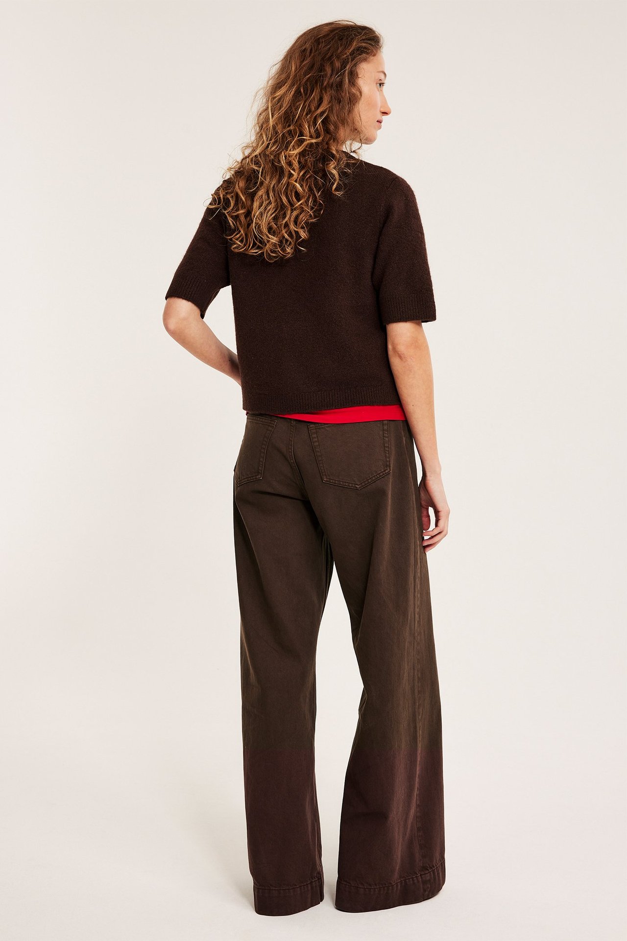 Bakfra: kvinne i mørkebrune vide jeans, mørkebrun kortermet topp og rød t-skjorte.