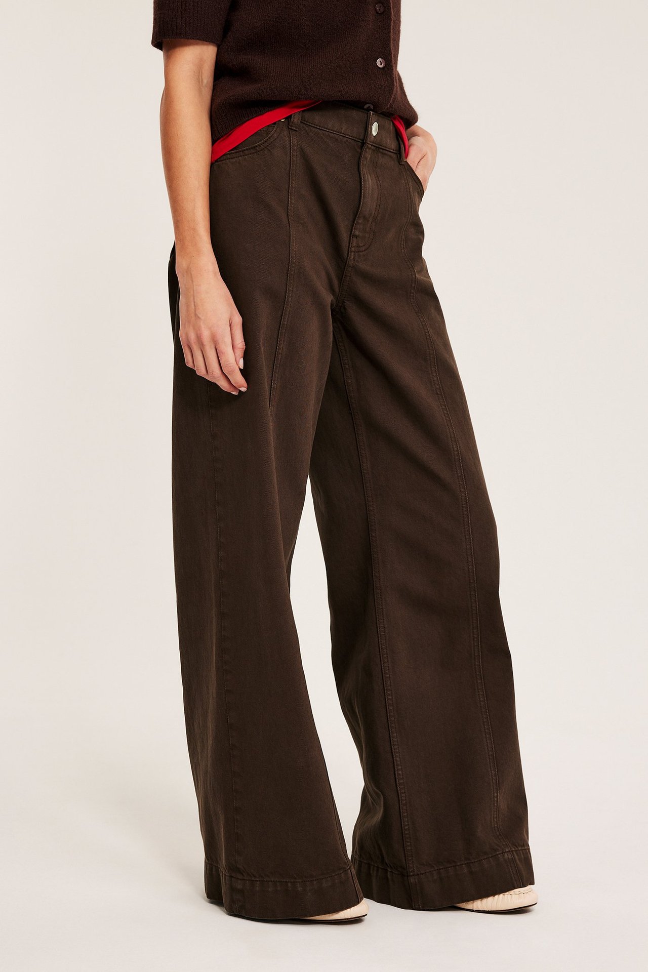 Forfra: Kvinne i mørkebrune vide twill-jeans med sømmer foran, stylet med en brun cardigan.