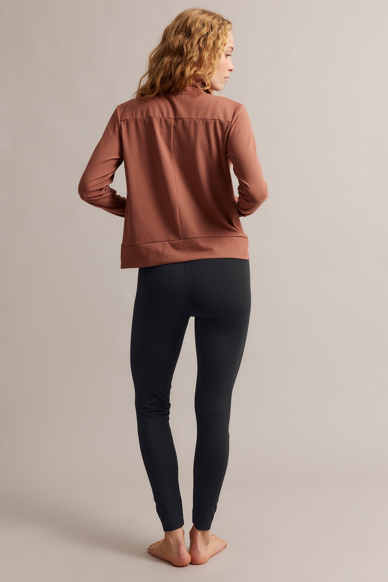 Bakifrån på kvinna i svarta leggings med hög midja och en rostbrun långärmad topp.