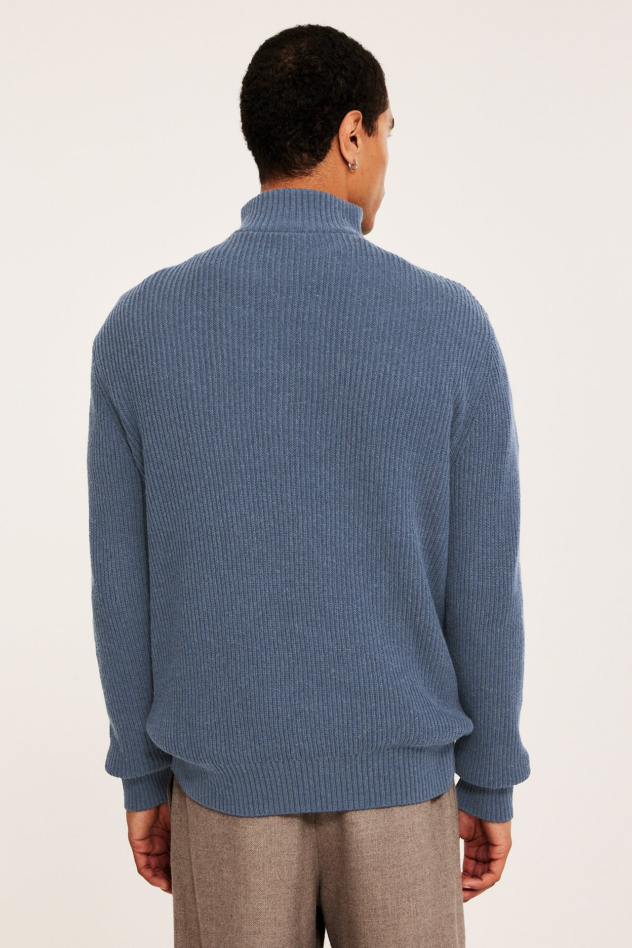 Mies takaa, yllään sininen meleerattu ribbineule half-zip-villapaita ja ruskeat housut.