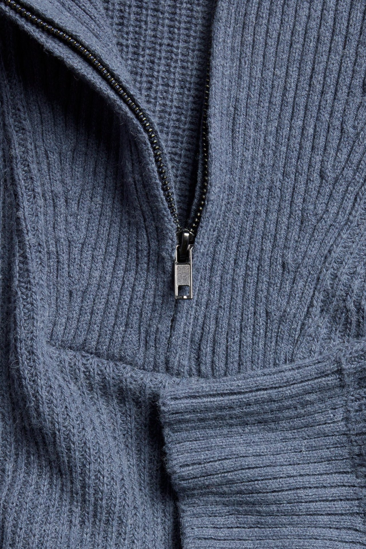Zbliżenie na niebieski melanżowy sweter dzianinowy z półzamkiem, prążkowaną fakturą i srebrnym suwakiem.