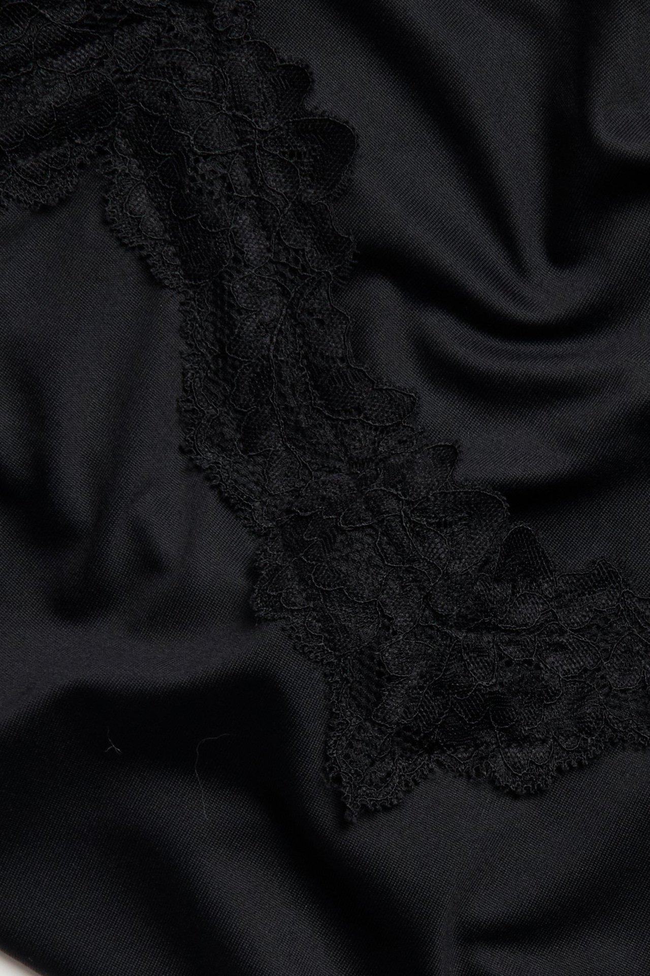 Zbliżenie czarnego, dopasowanego topu na ramiączkach z delikatną koronkową lamówką.
