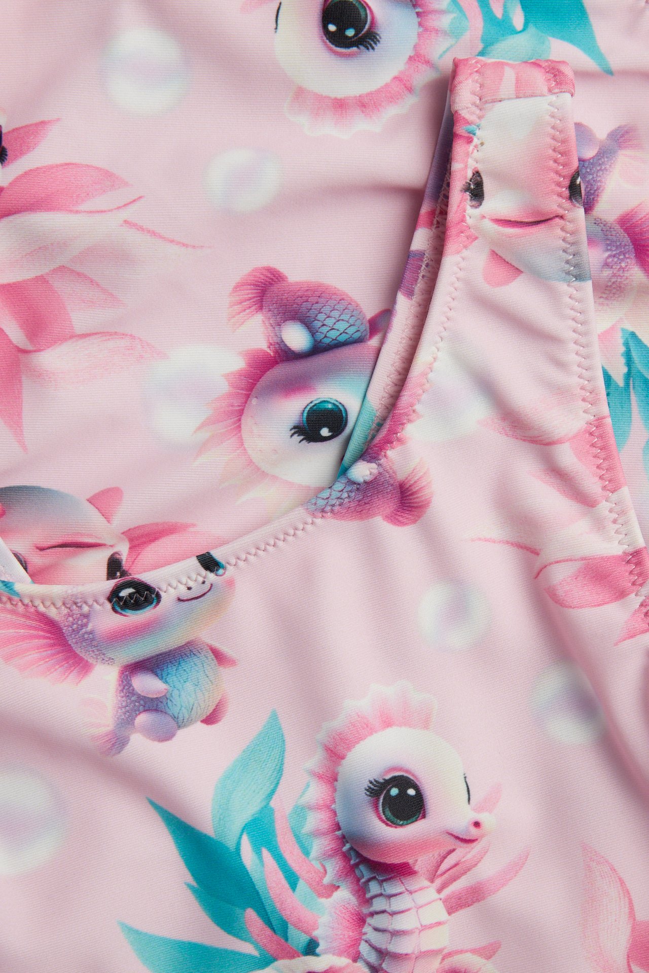 Närbild på en rosa mönstrad baddräkt för barn med tecknade sjödjur och bubblor.