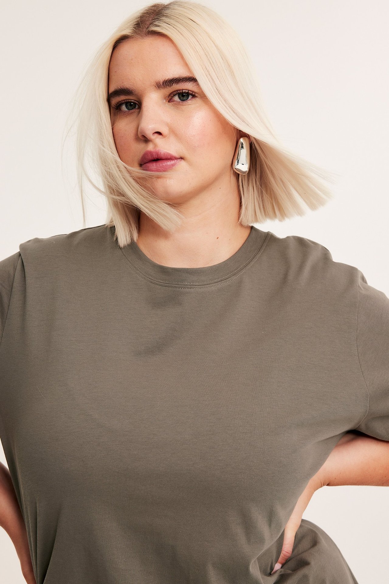 Zbliżenie z przodu kobiety w luźnym brązowym bawełnianym długim t-shircie i jednym srebrnym kolczyku.