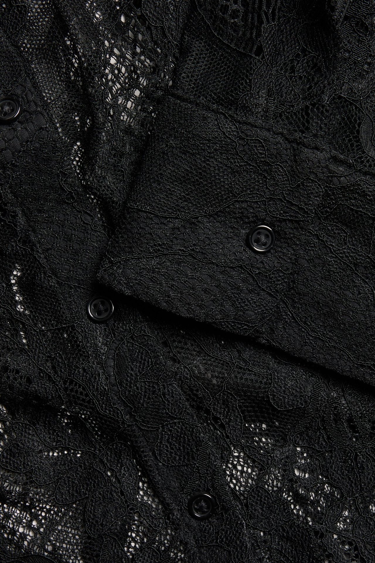 Zbliżenie czarnej koronkowej koszuli z misternym kwiatowym wzorem i zapięciem na guziki.