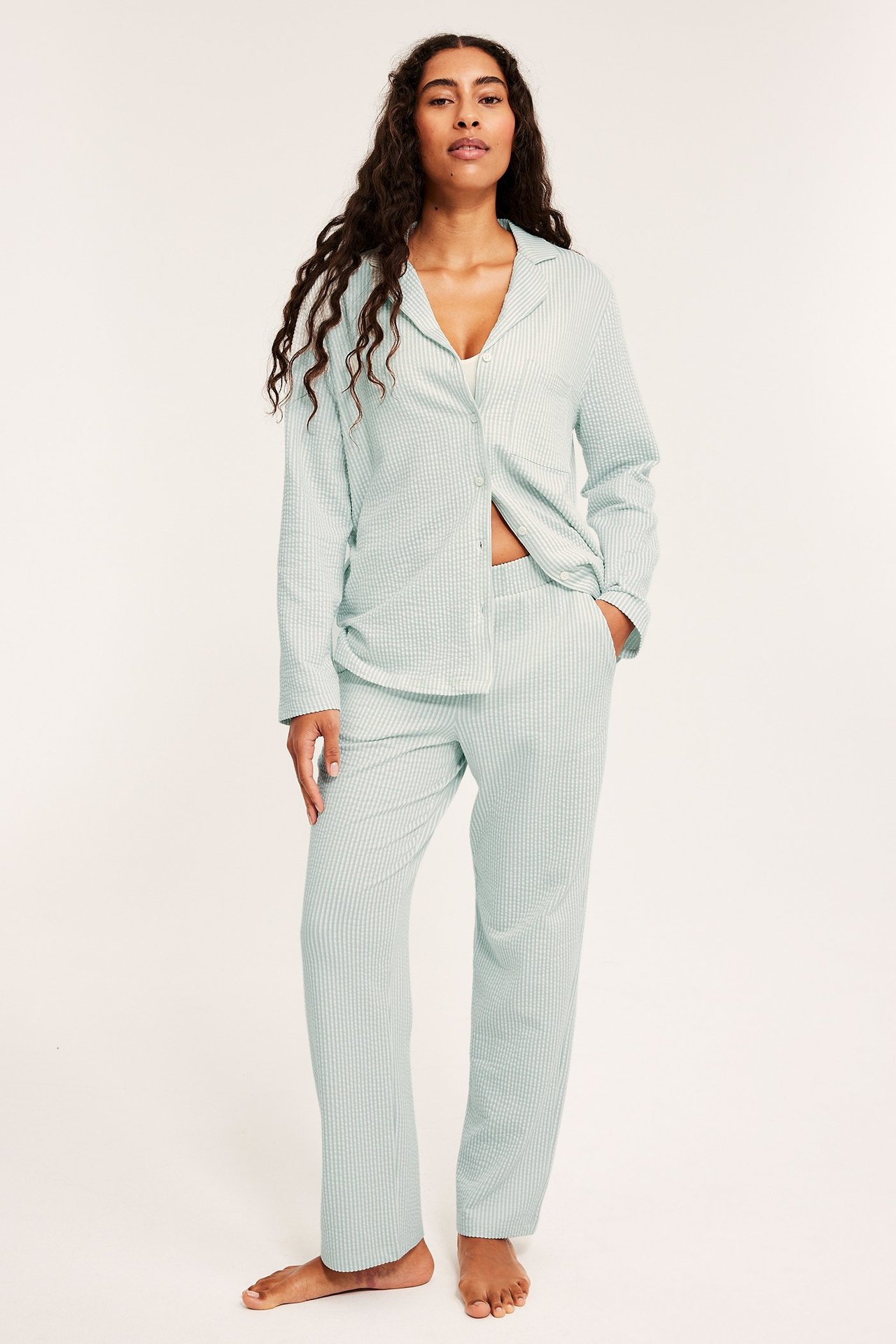 Kobieta w jasnozielonych, pasiaste pyjamasach z kieszenią na piersi i elastycznymi spodenkami.