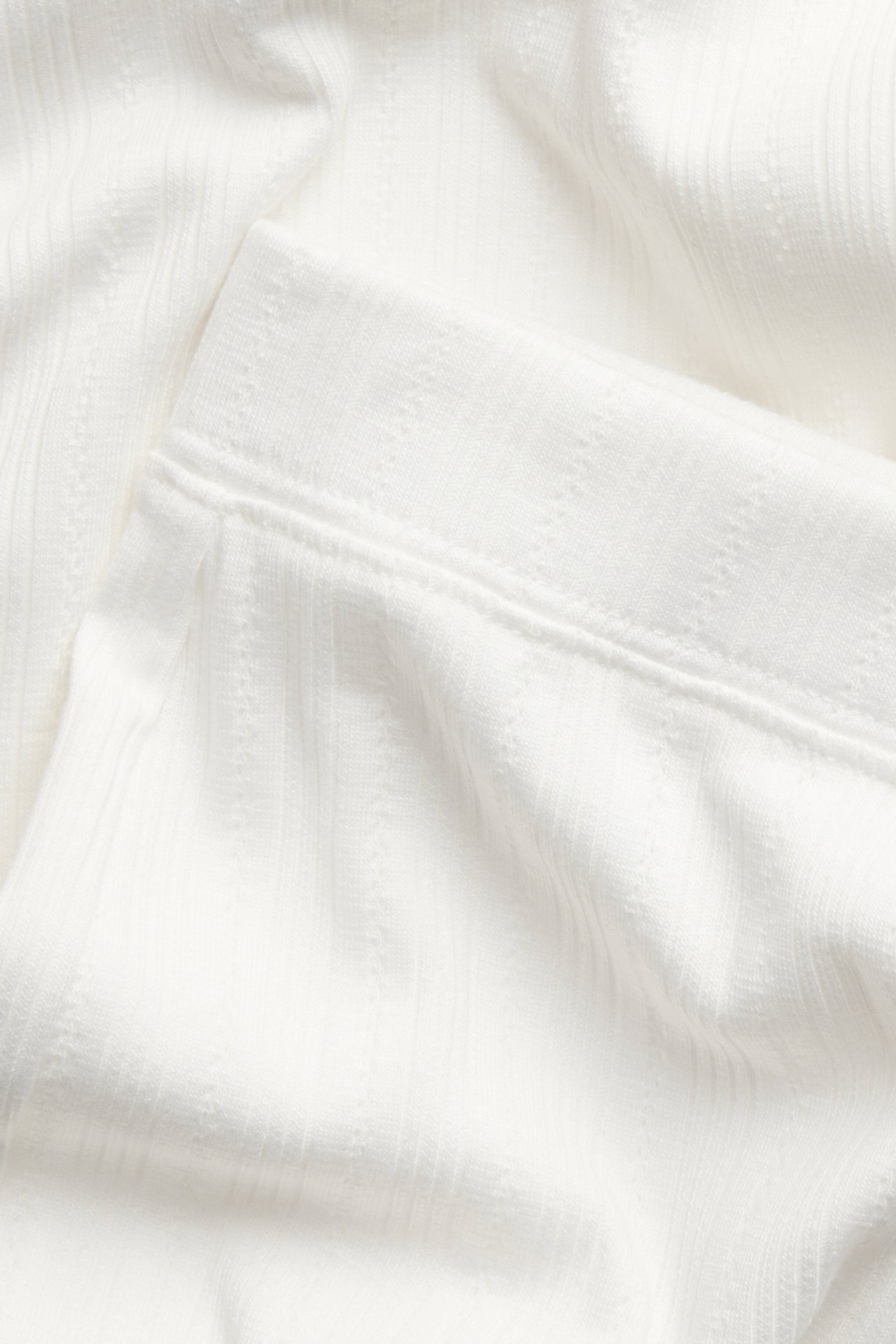 Närbild av offwhite ribbade pyjamasbyxor i jersey med resår i linningen.