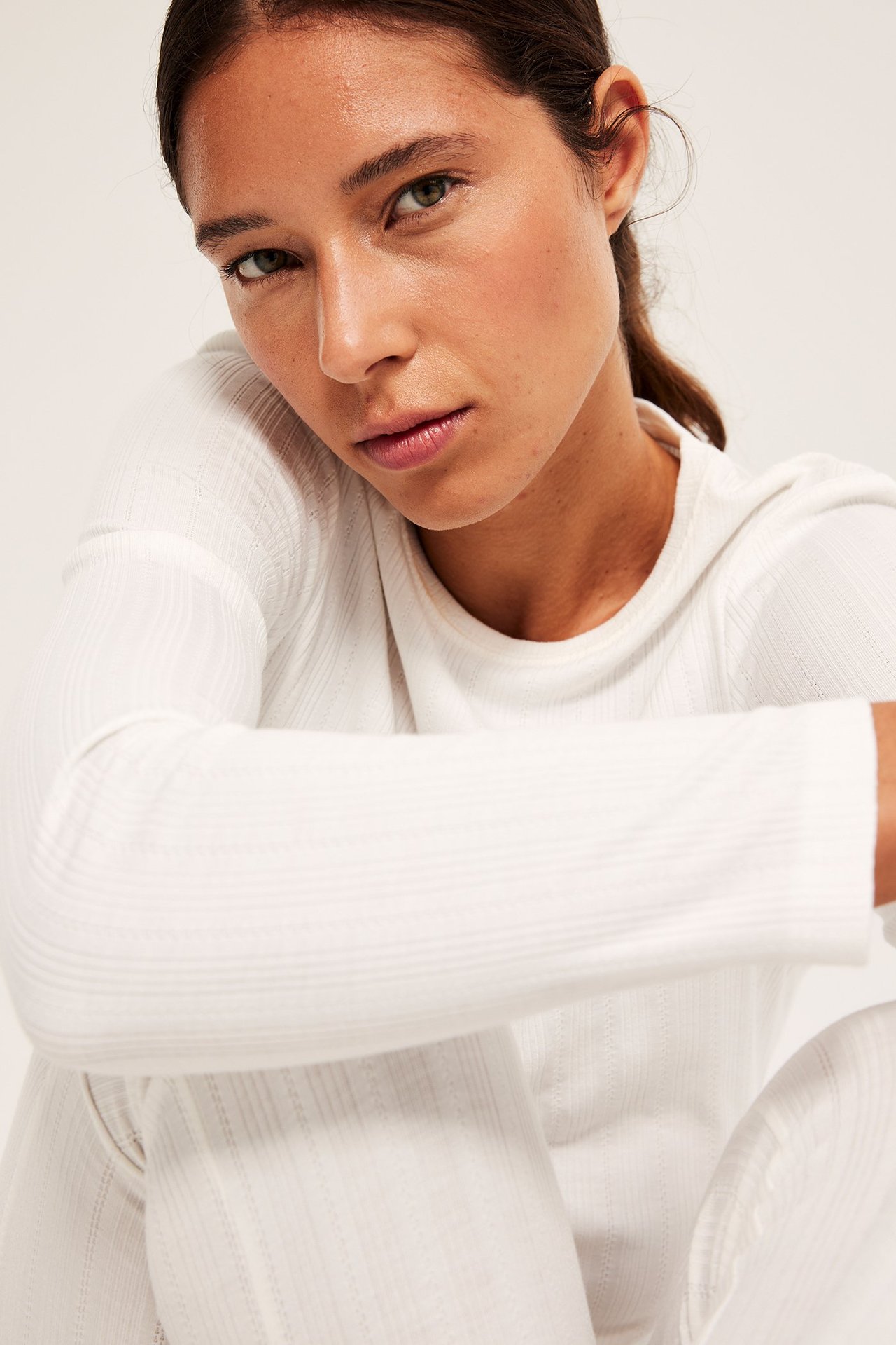 Zbliżenie kobiety w kremowej, długiej bluzce piżamowej w prążek i pasujących spodniach.