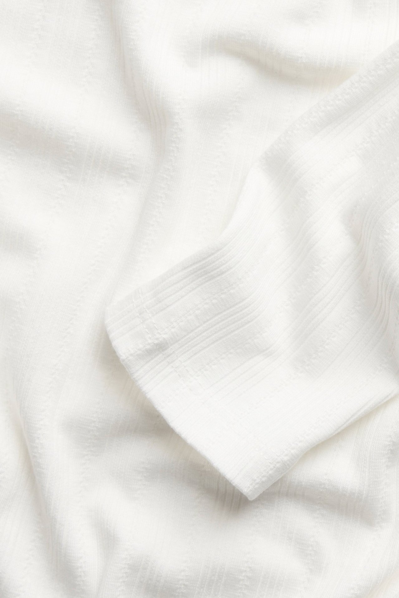 Zbliżenie tkaniny piżamy w kolorze off-white, z prążkowaną fakturą i subtelnym wzorem.