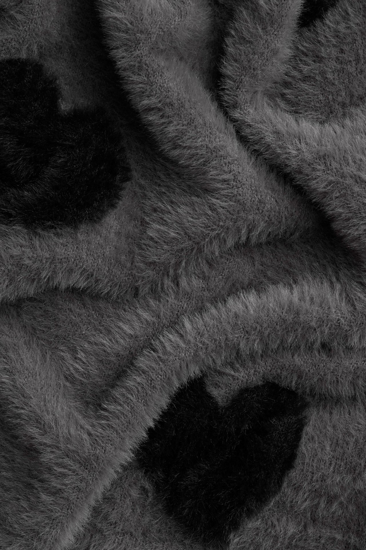 Zbliżenie miękkiego szarego swetra z przędzy piórkowej z czarnymi sercami żakardowymi.